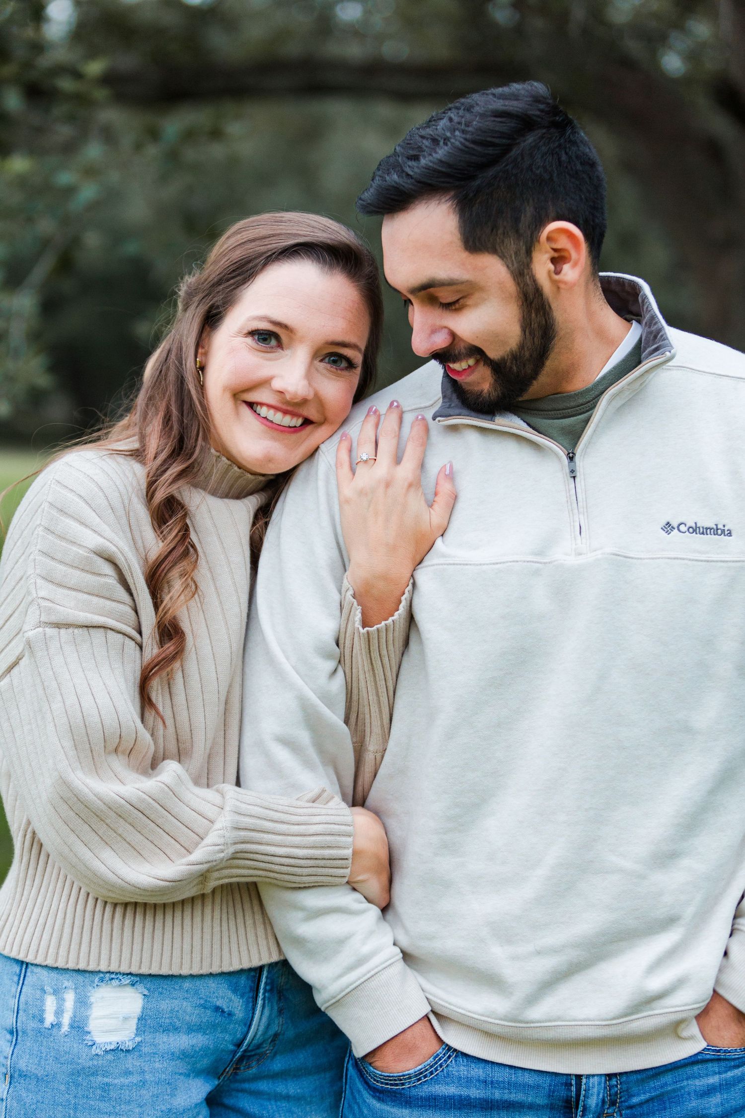 Couple in cream sweaters and jeans embracing outdoors.
