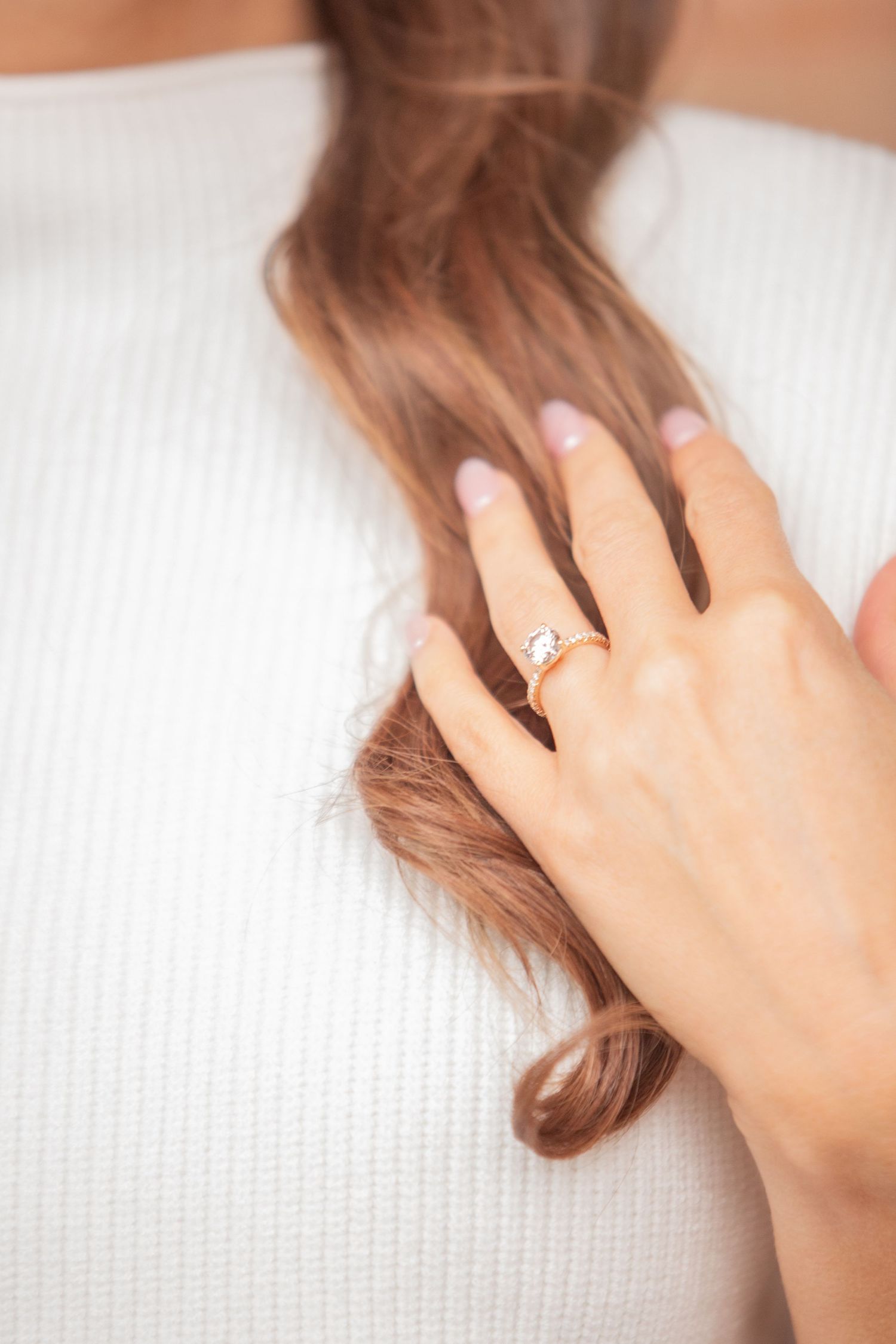 Close up of diamond engagement ring on woman's hand against white fabric.