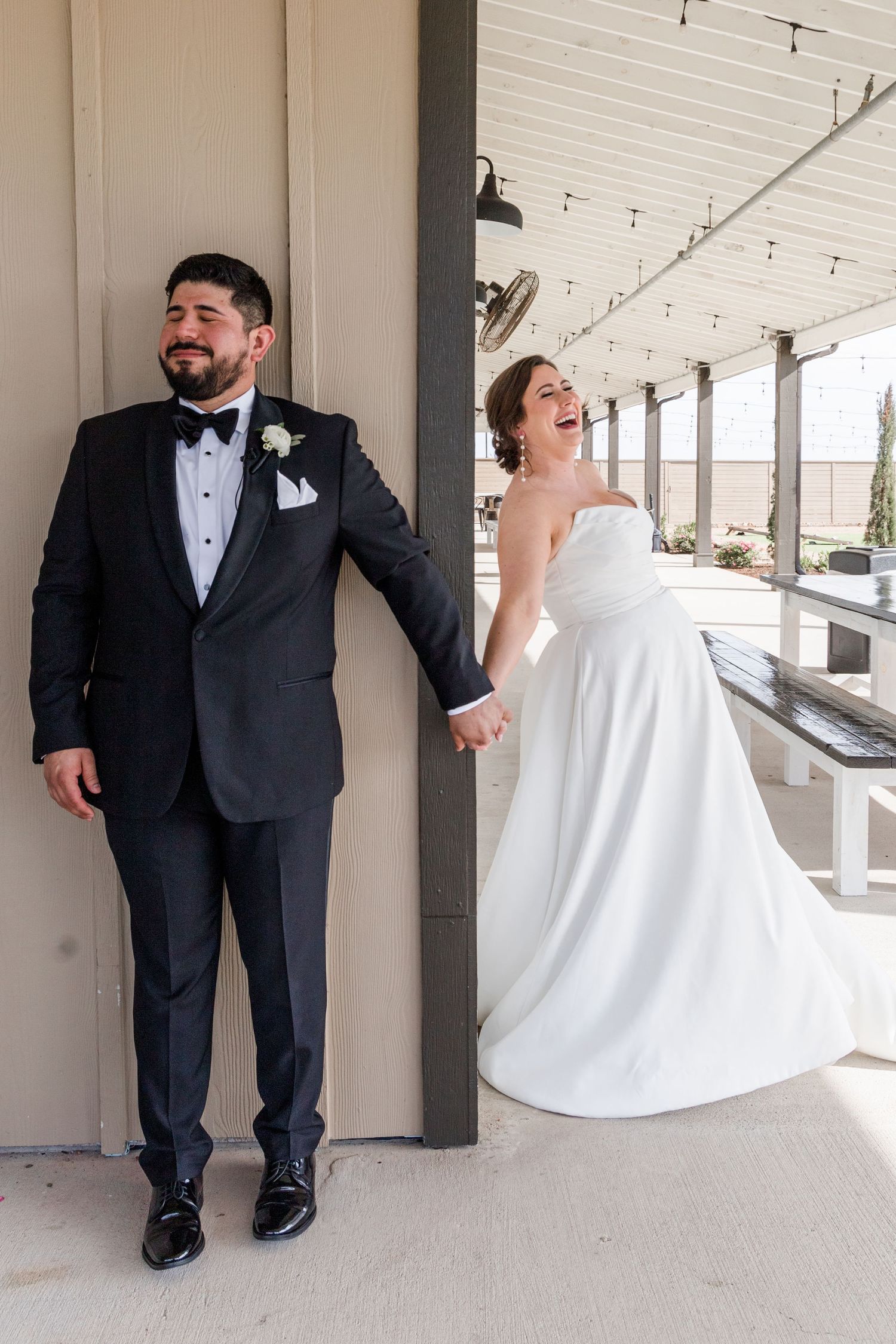 Joyful wedding couple sharing a laugh while standing on opposite sides of a pillar.