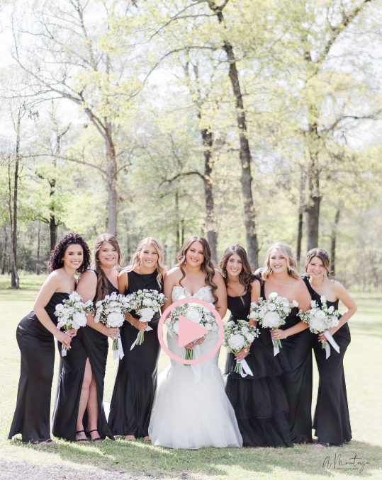 Bridal party in black dresses poses with bouquets outdoors.