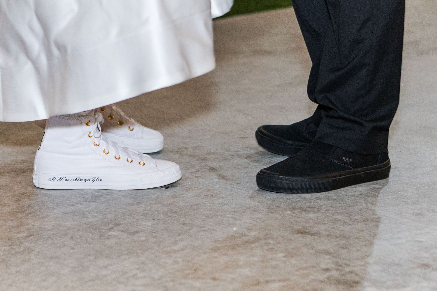 Close-up view of formal wedding shoes with the bride wearing white sneakers and groom in black dress shoes.