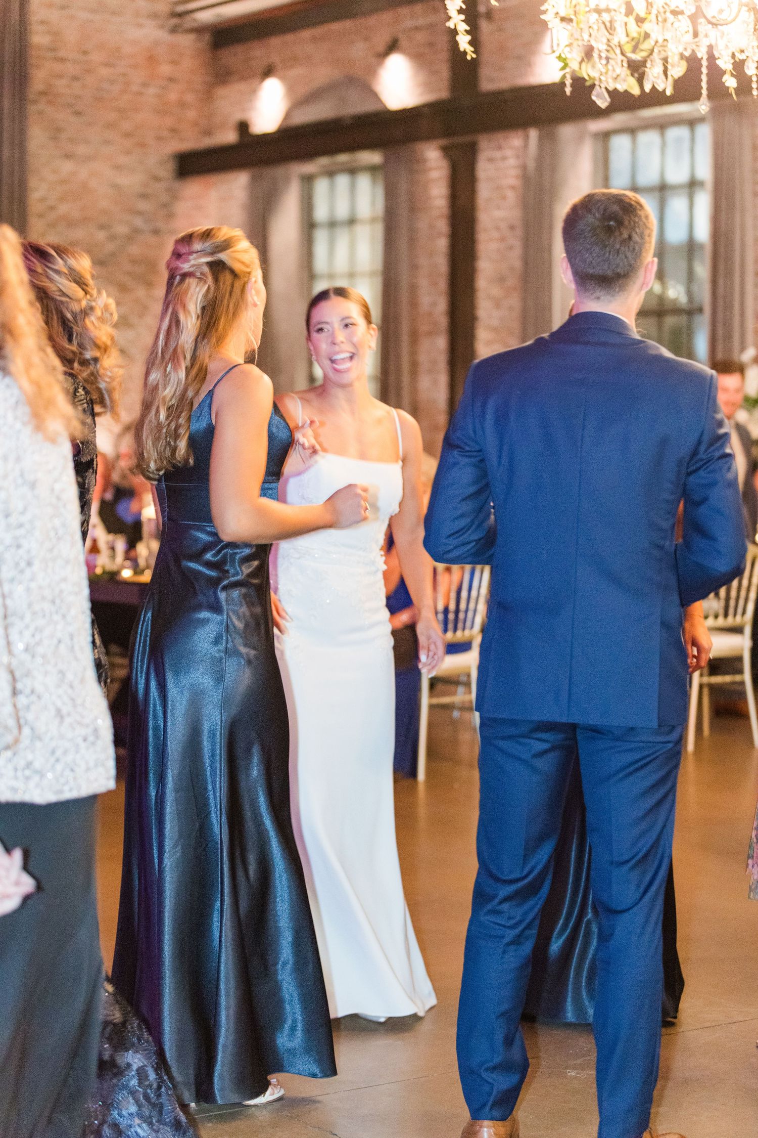 Wedding guests in navy and white formal attire dancing in an industrial-style venue.