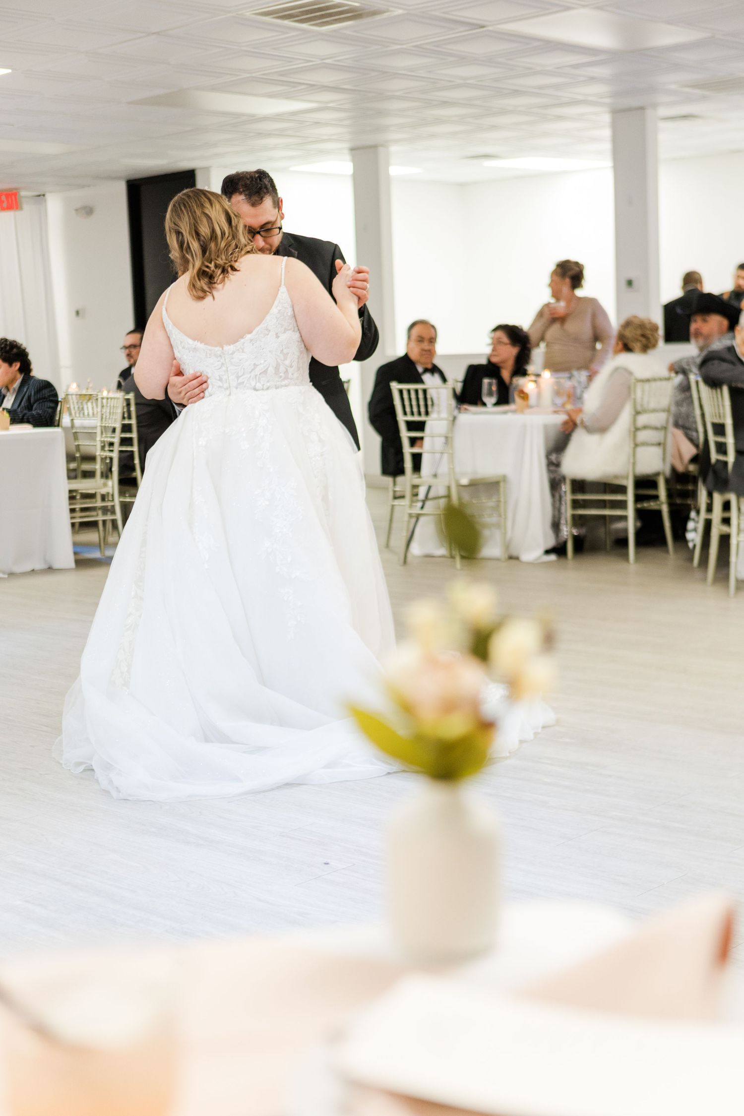 A couple shares their first dance at a wedding reception in a bright white venue with elegant decor.