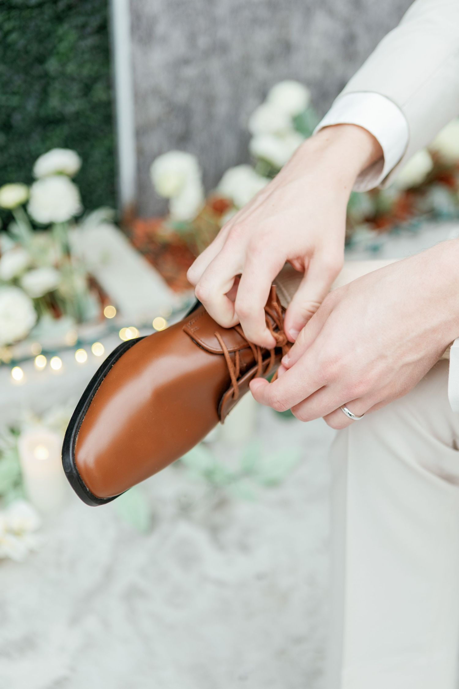 Hands lacing up brown leather dress shoes during wedding preparations.