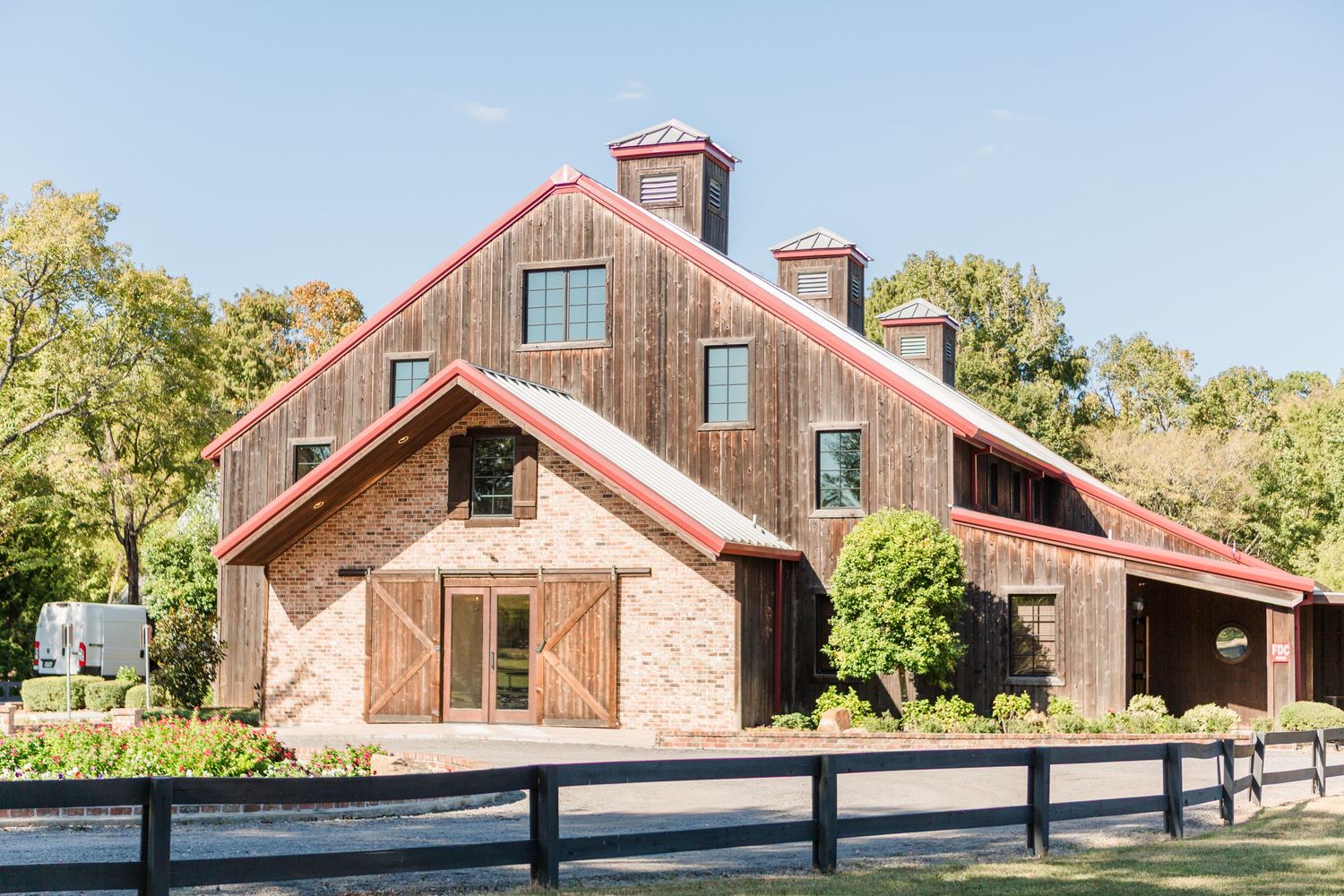 Rustic barn-style wedding venue with wood and stone exterior features black fencing and natural landscaping.