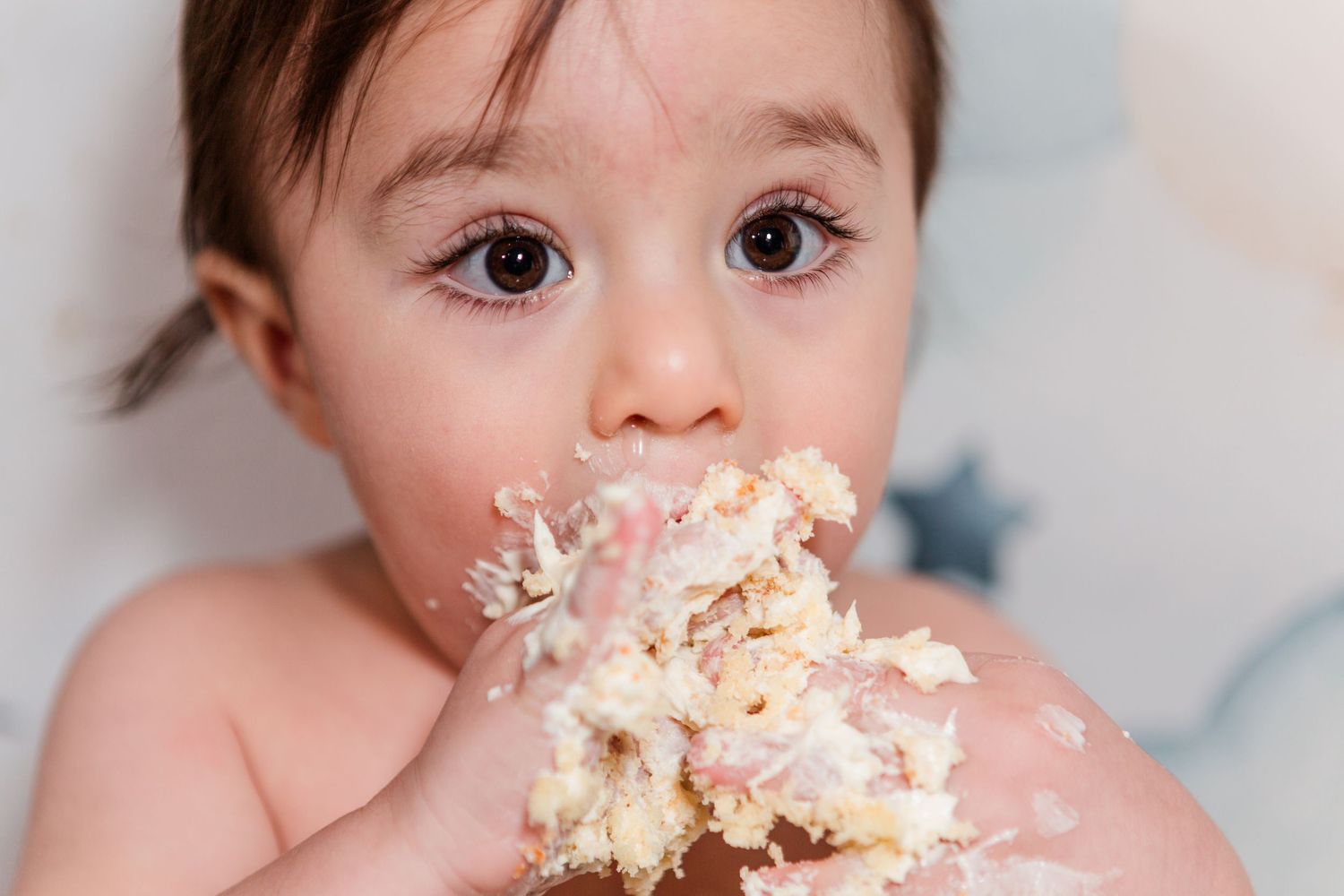 Baby covered in white cake frosting during first birthday celebration.