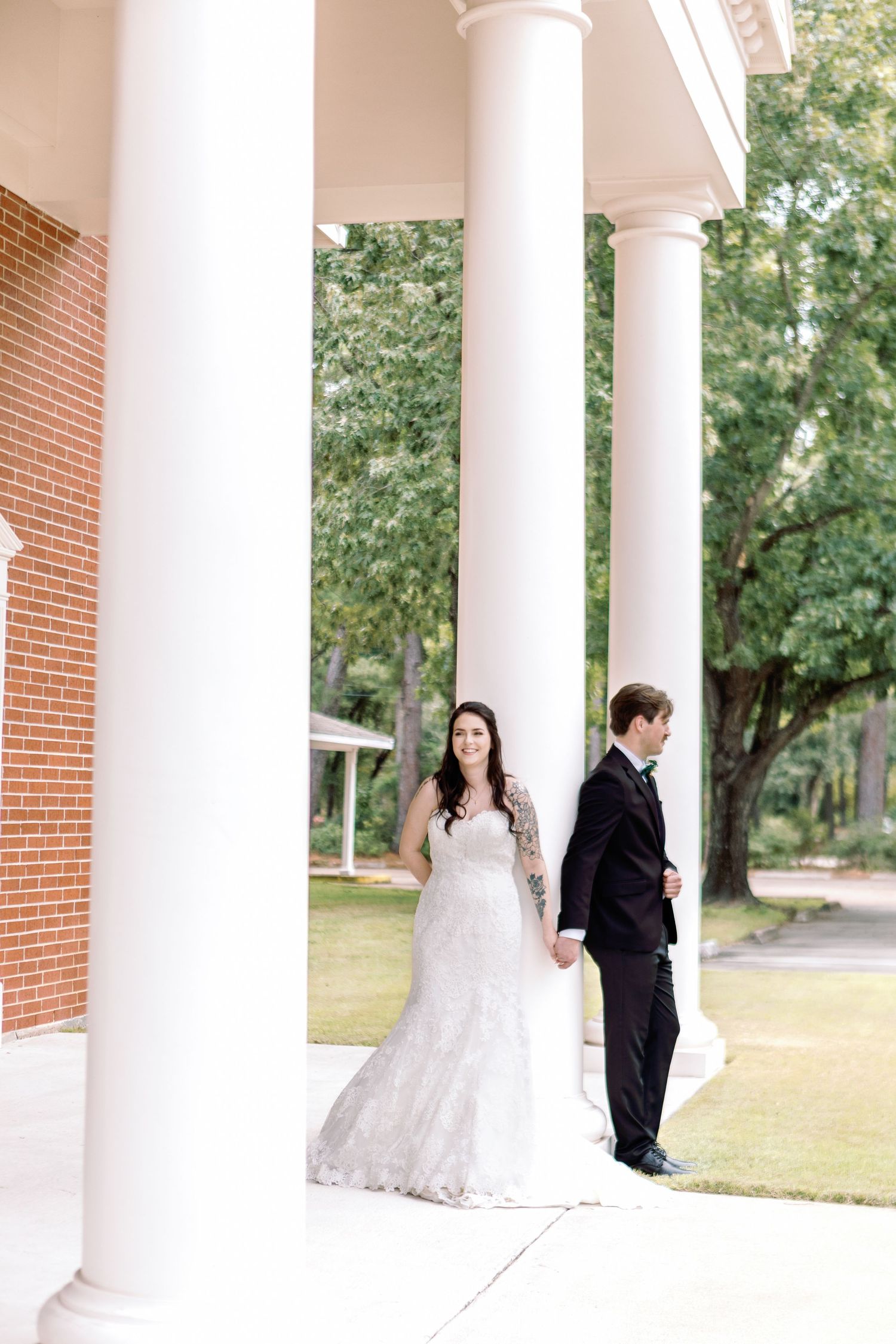 A bride and groom stand apart between elegant white columns during their first look moment.