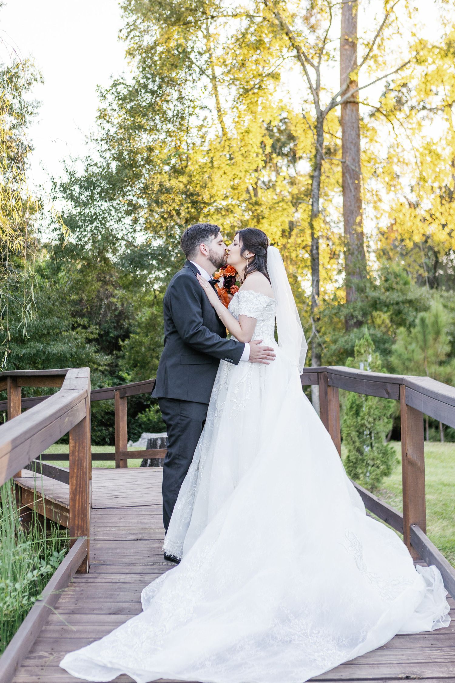 A romantic wedding couple shares intimate moments on a wooden bridge surrounded by golden autumn trees.