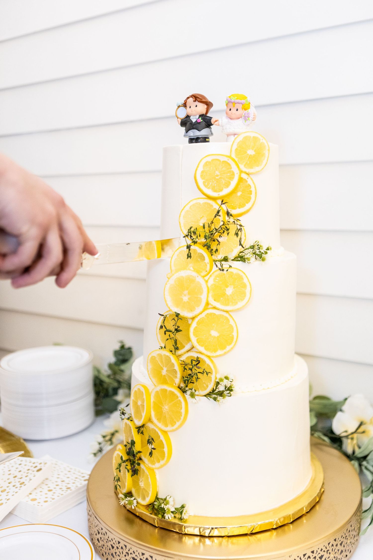 White wedding cake decorated with fresh lemon slices and greenery on a gold cake stand.