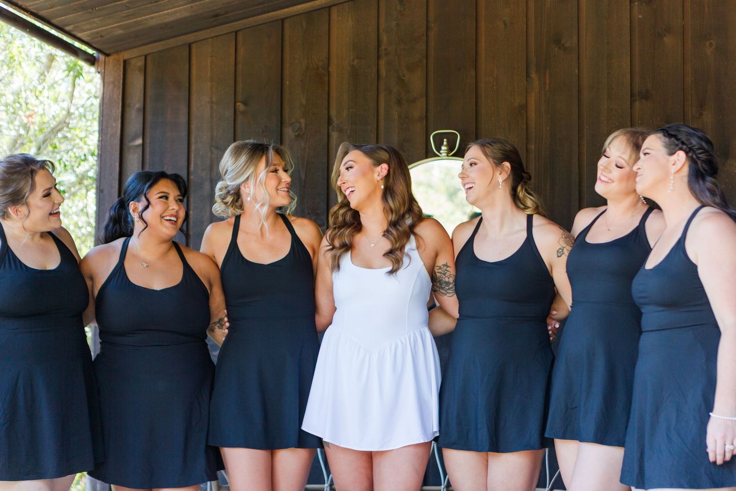 Row of bridesmaids in matching navy dresses standing in a rustic wooden venue.