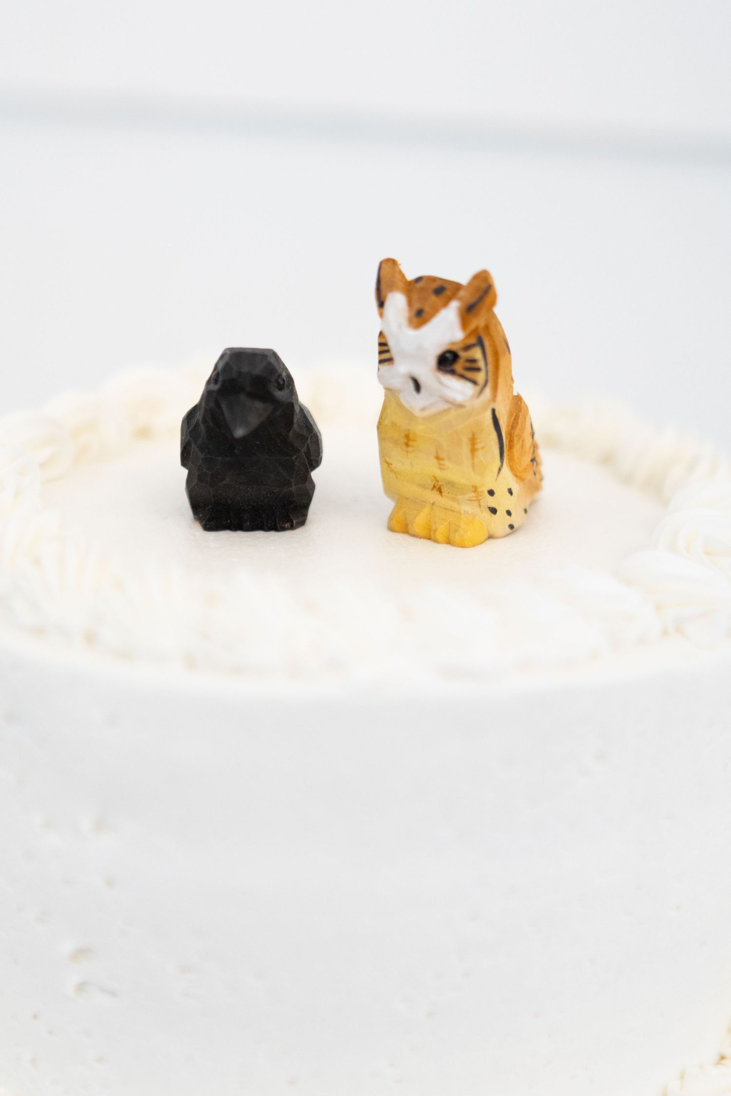 Cat and black rock wedding cake toppers sit atop white frosting against a light background.