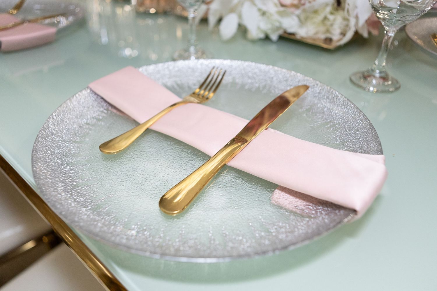 Close-up of elegant place setting with silver charger plate, pink napkin, and gold cutlery.