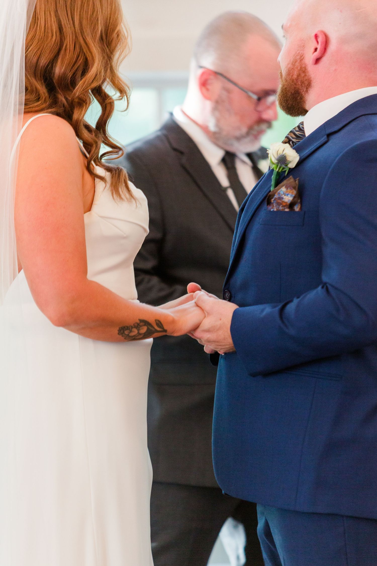 Wedding ceremony participants wearing formal attire standing in a bright indoor space.