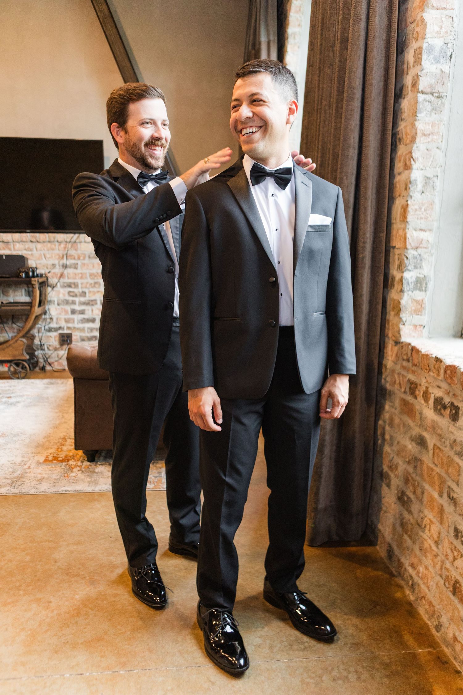 Wedding party members in tuxedos sharing laughs in an industrial-style venue.