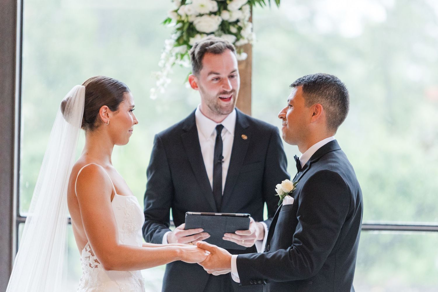 A special moment during an indoor wedding ceremony with sunlight streaming through large windows.
