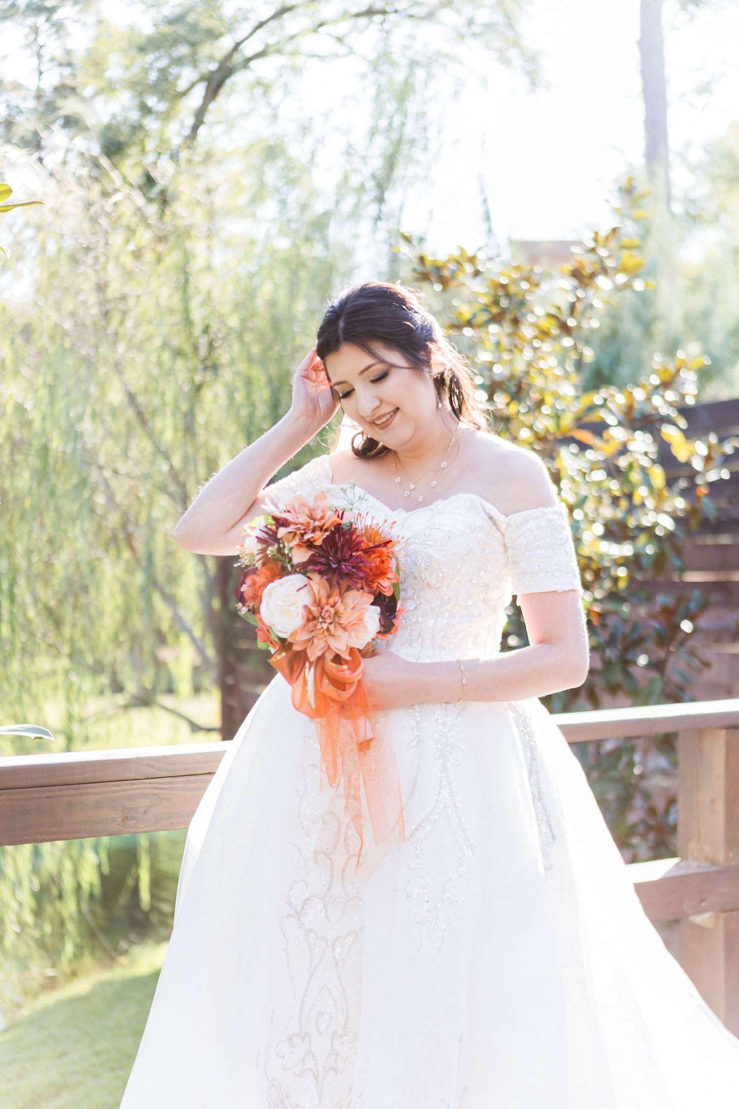 A bride in a white ballgown holds a vibrant orange and coral bouquet against an outdoor backdrop.
