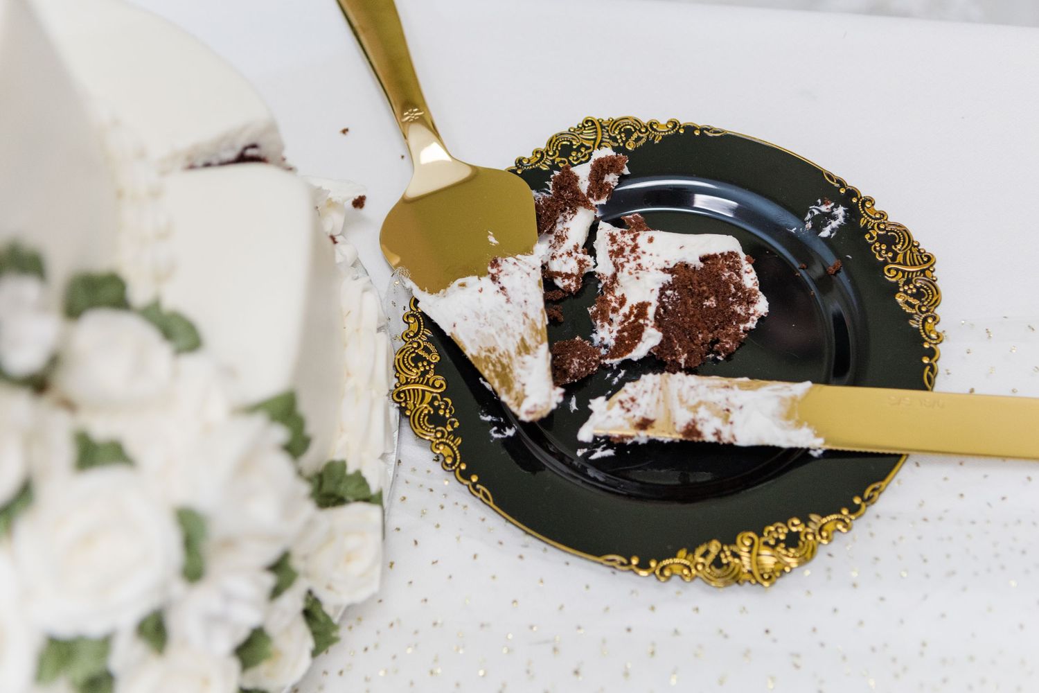 Wedding dessert being served with gold utensils on black plates with floral decor.
