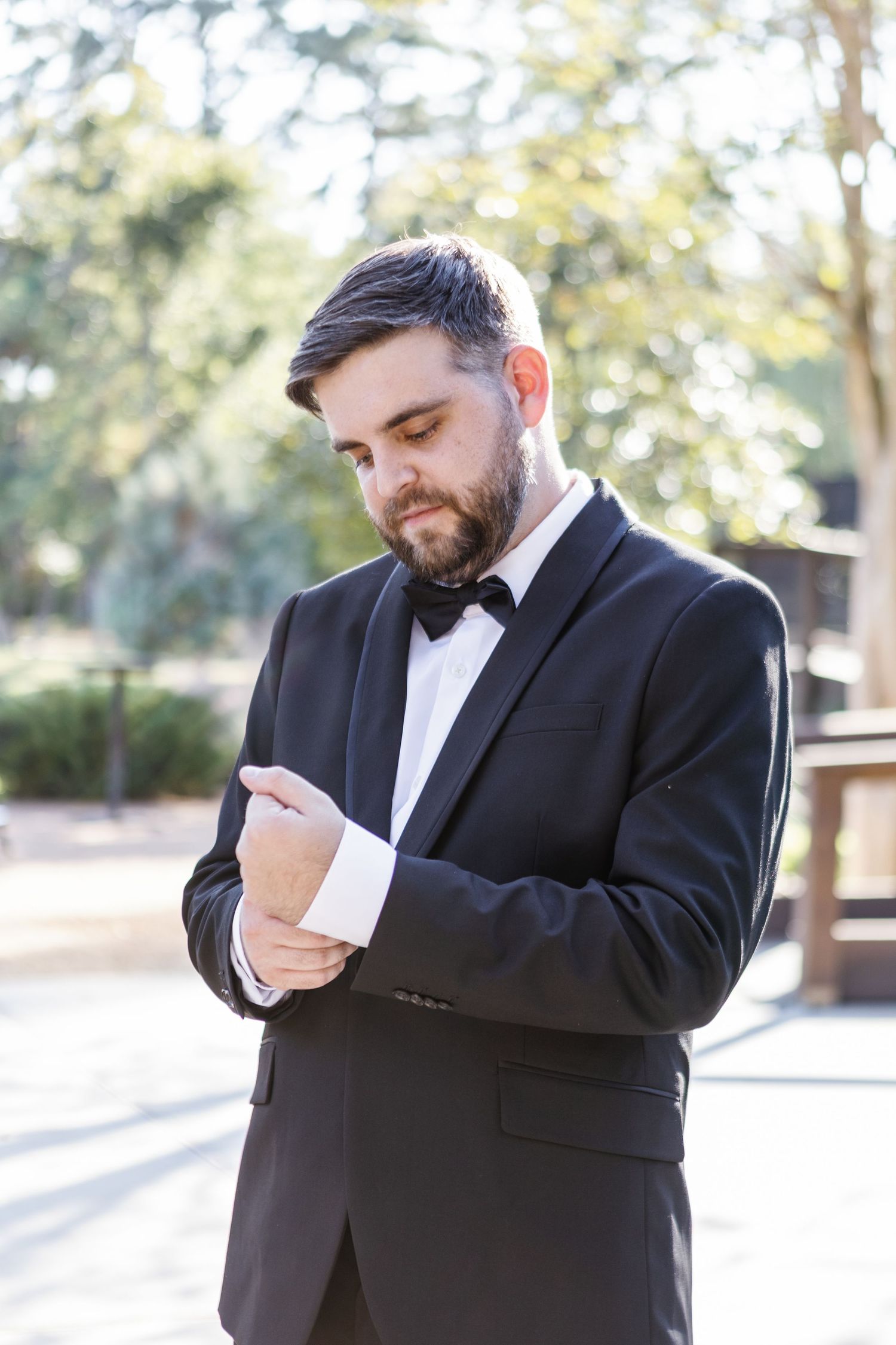 Groom in black tuxedo shows emotional reactions while reading a heartfelt note outdoors.