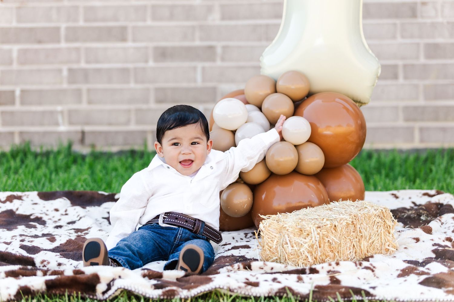 Baby photoshoot setup with rustic decor, balloons, and hay bales against brick wall.