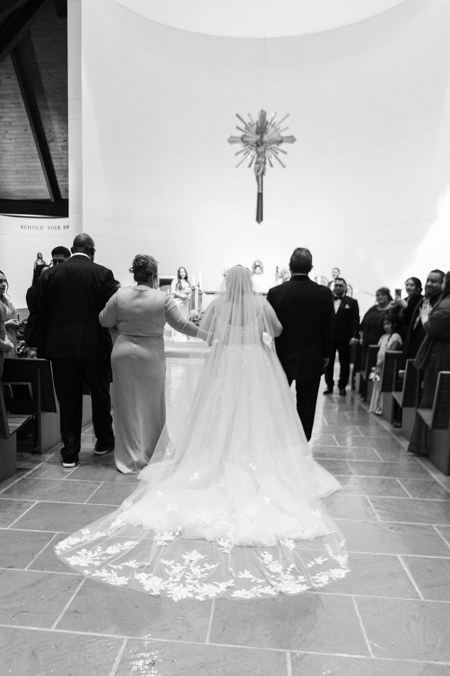 Black and white photo of a bride's cathedral veil stretching down a modern church aisle.
