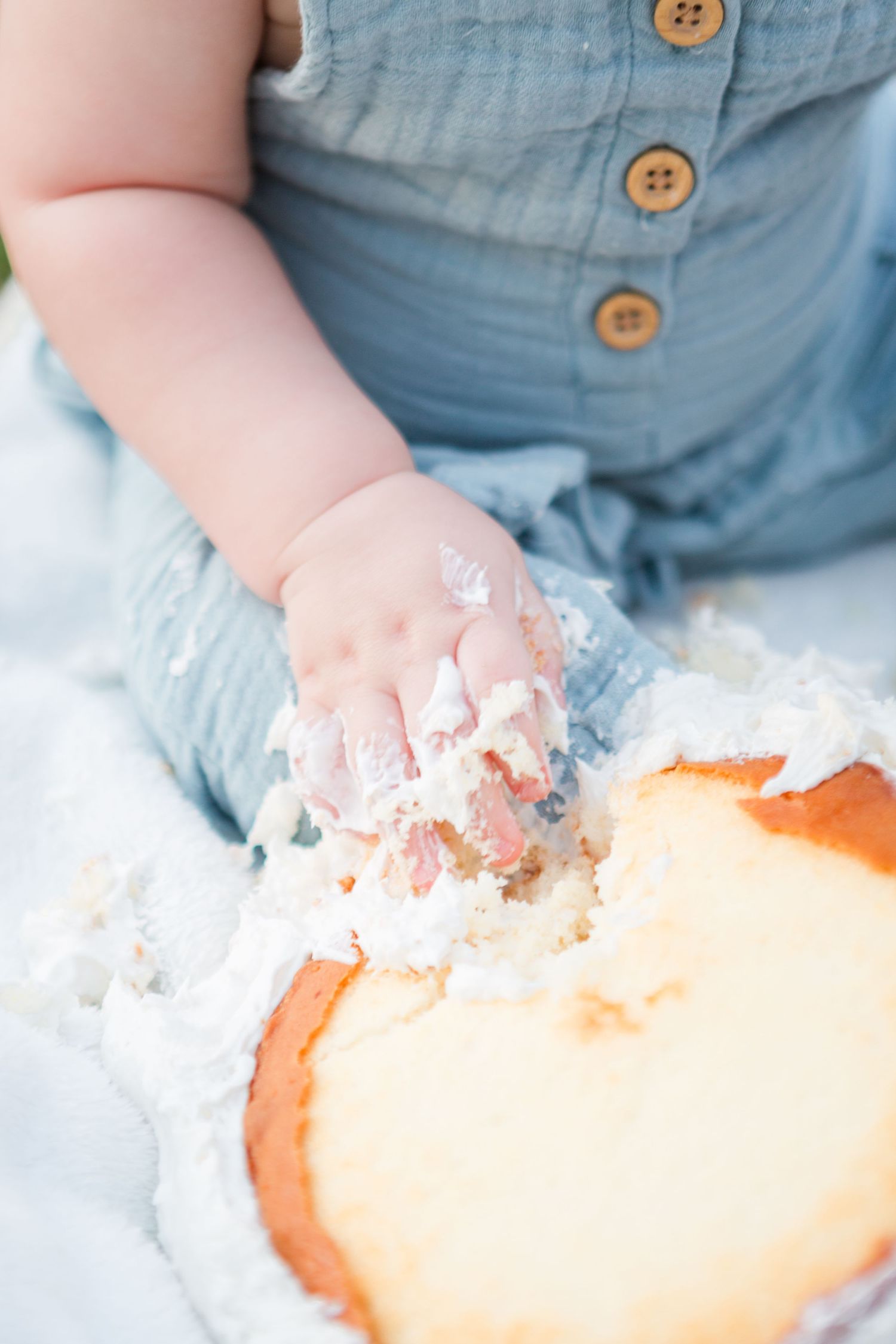 Close-up of small hands playing with cake frosting during a smash cake session.