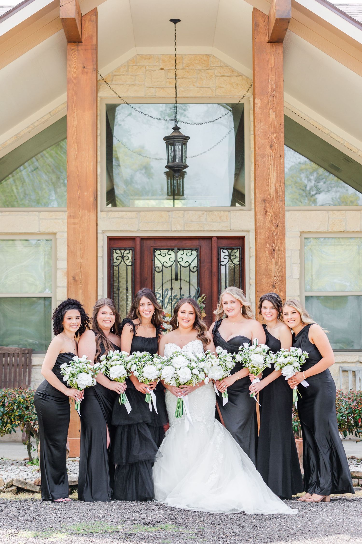 Wedding party poses under wooden beams at rustic venue entrance.