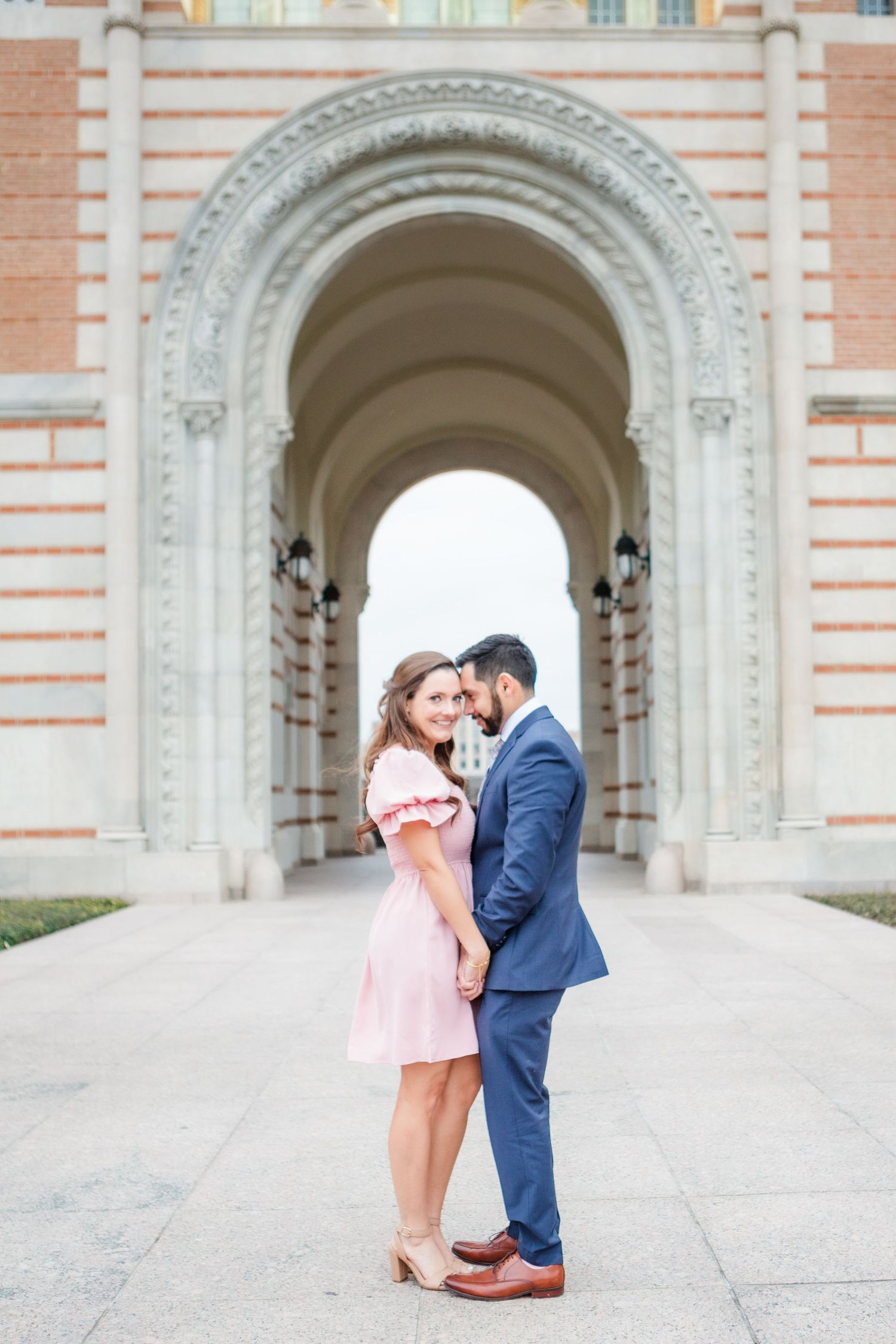 A couple stands together under ornate archways of a historic building.