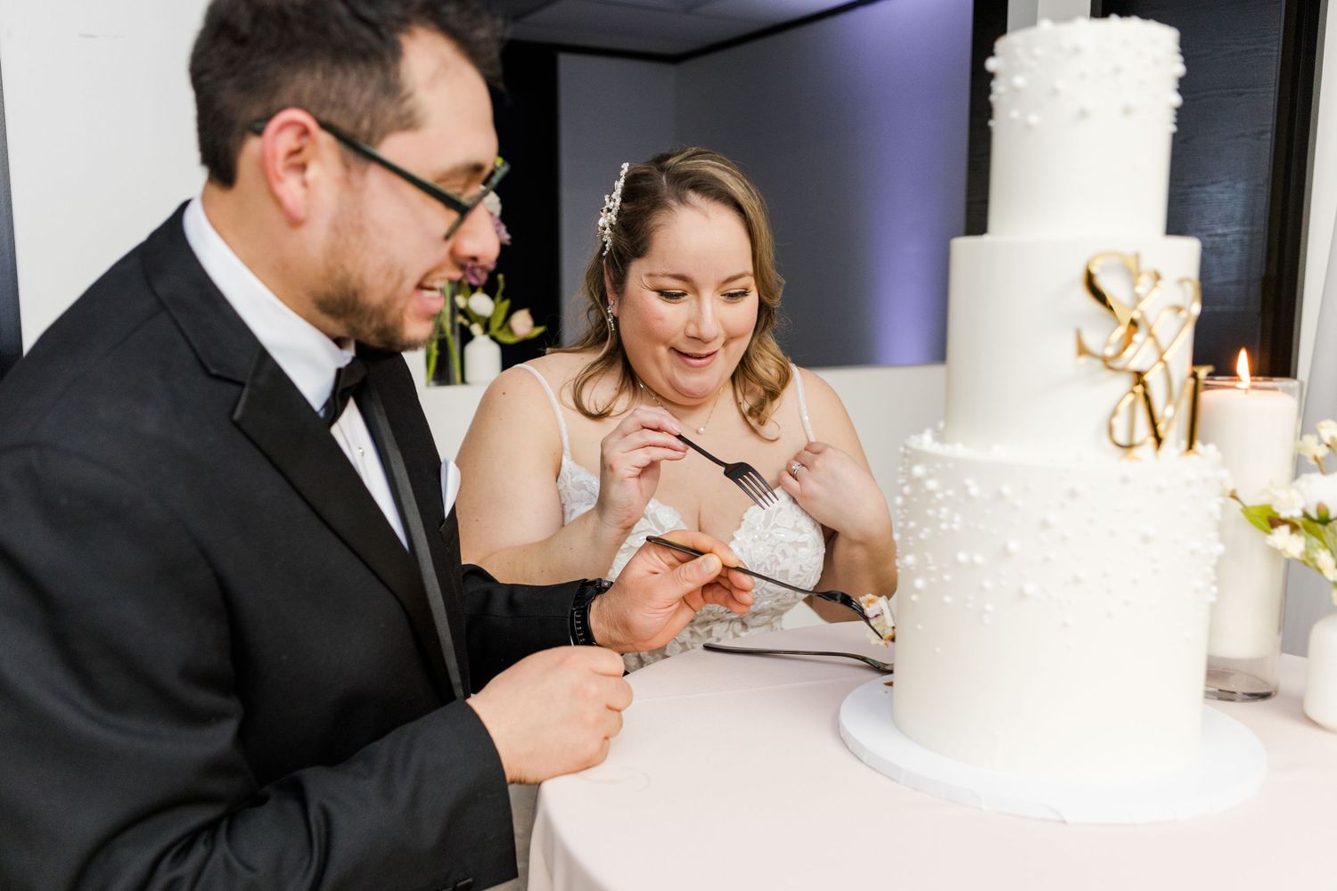 Elegant tiered white wedding cake with intricate pearl detailing at a reception.