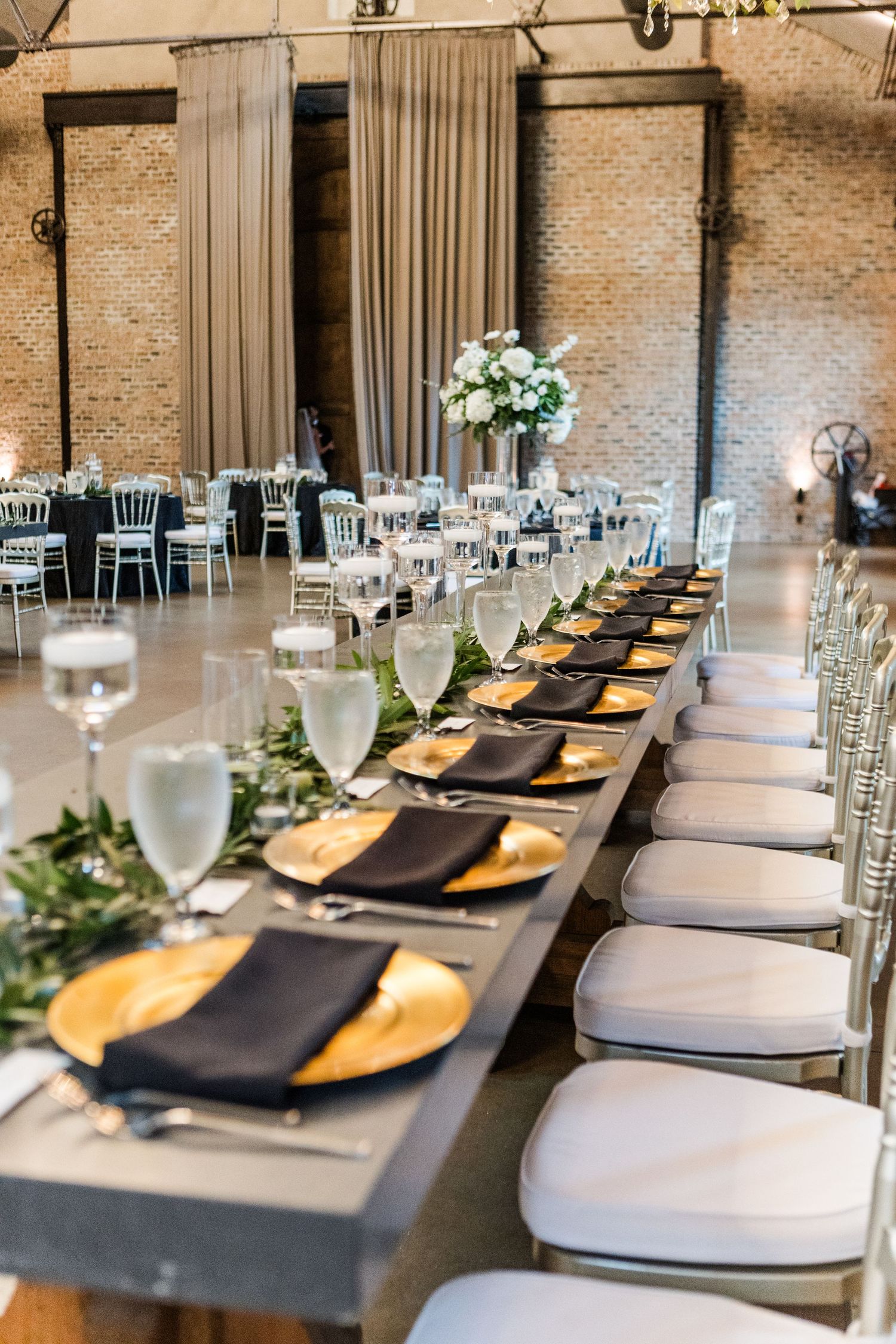 Elegant wedding reception table setting with black napkins and gold chargers in an industrial venue.