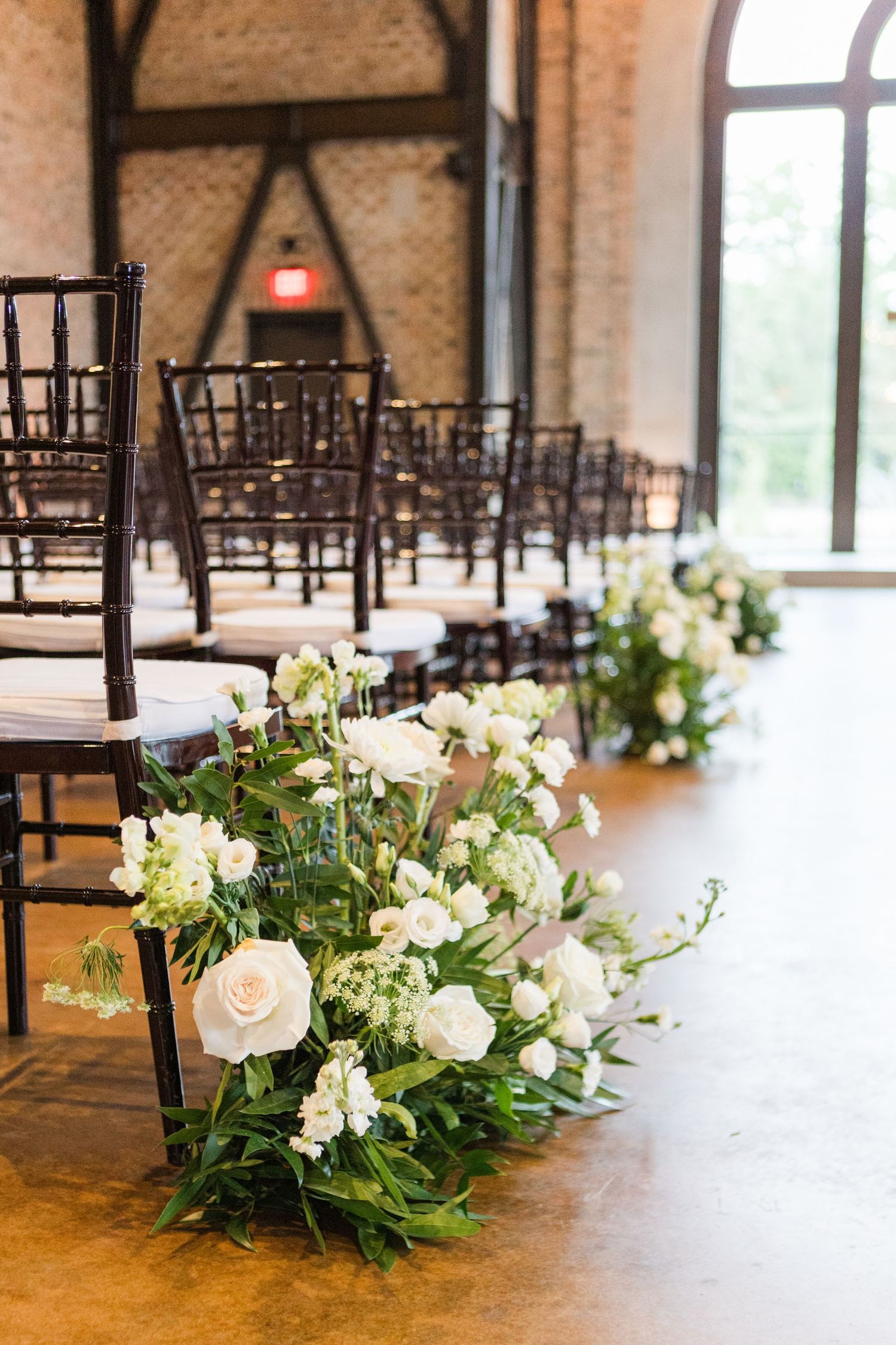 Dark wooden chairs lined up for wedding ceremony with white floral aisle decorations.