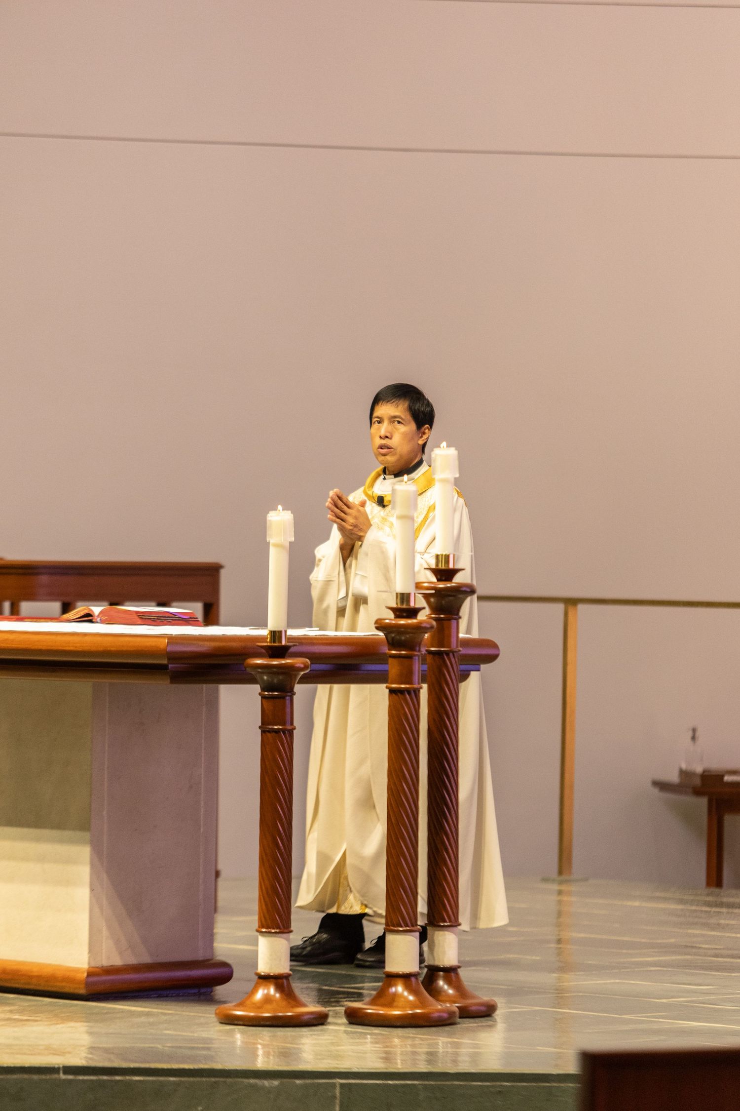 Priest in white robes conducts a religious ceremony at the altar.