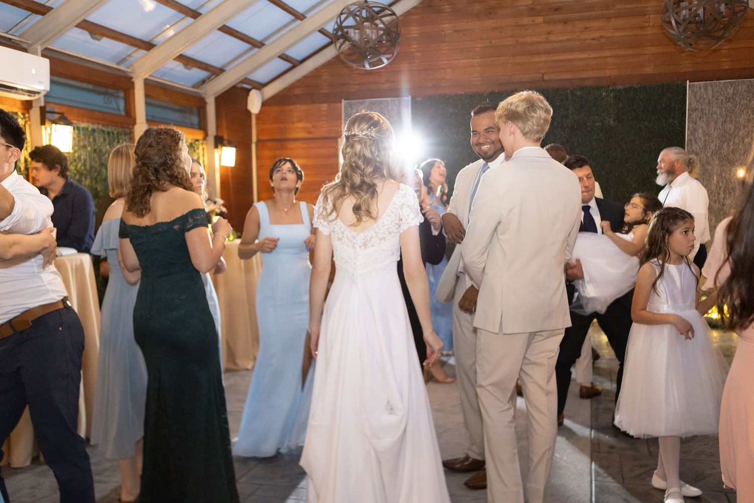 Lively wedding reception scene with multiple couples dancing under skylights and wooden beams.