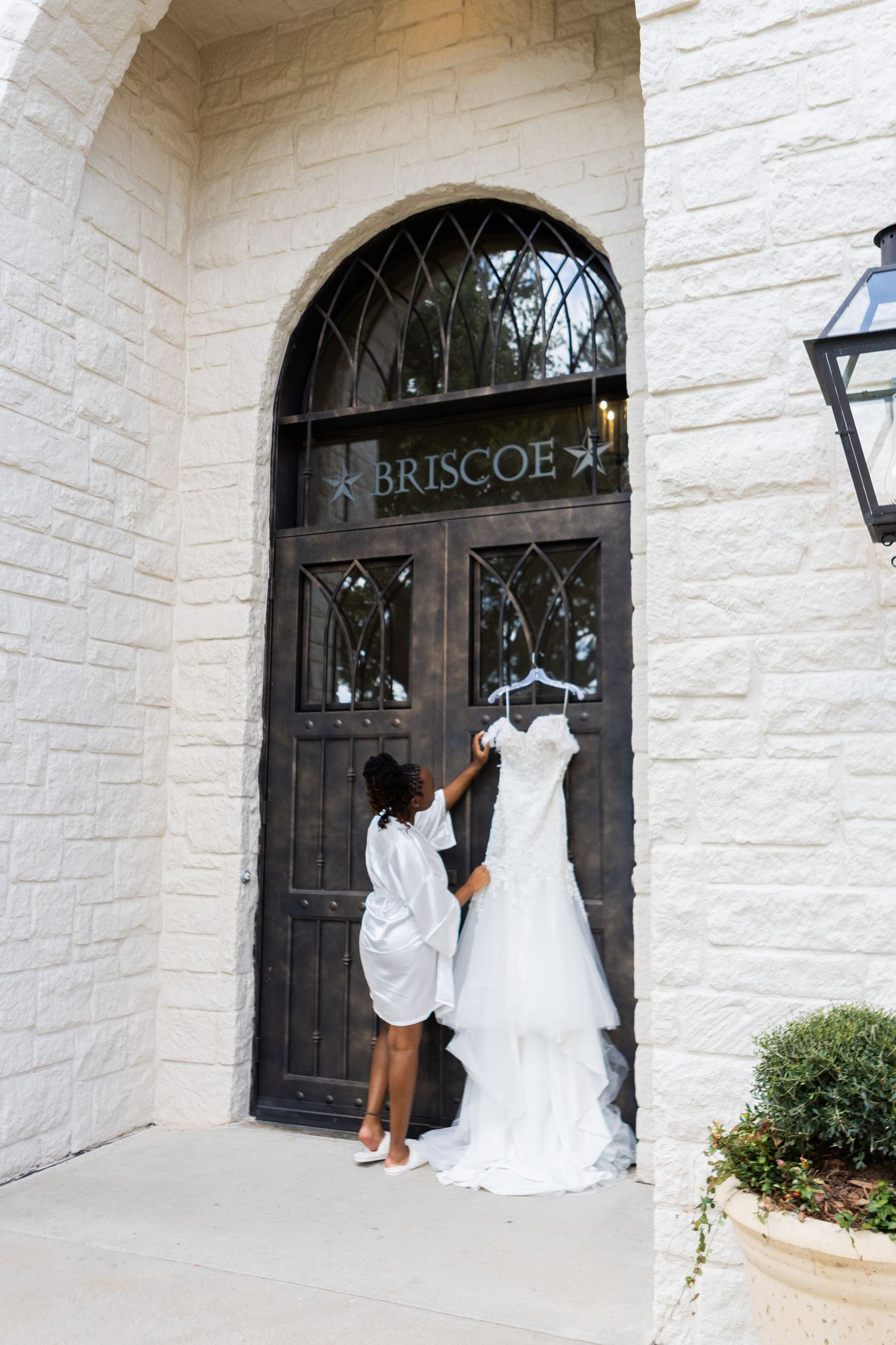 A wedding dress hangs on display at the entrance of Briscoe venue with white stone walls and an arched doorway.