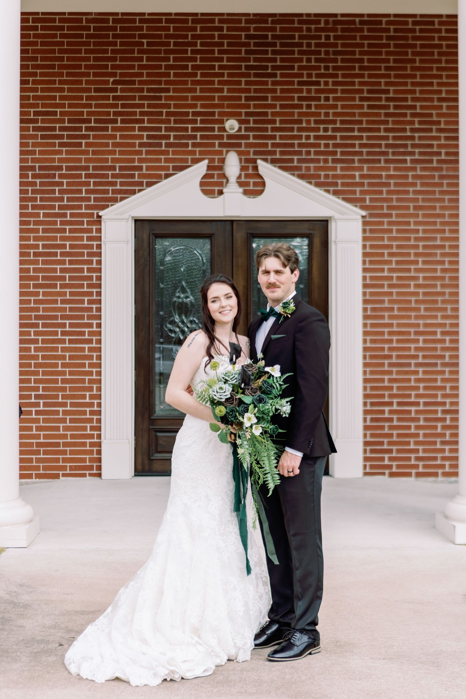 Wedding couple poses for portraits against a brick building exterior with white columns.