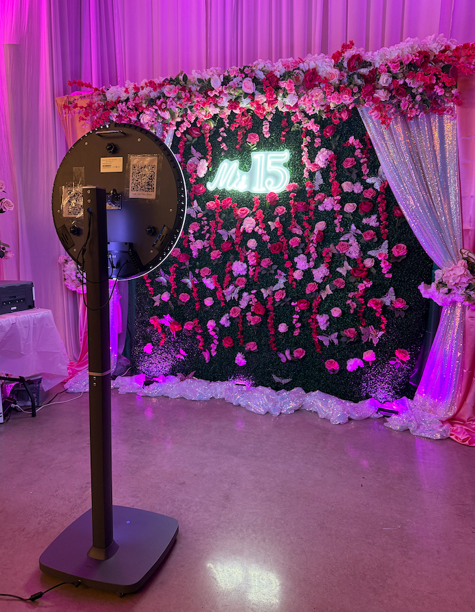 A row of four professional photo booth setups with pink floral backdrops and purple lighting for an elegant event.
