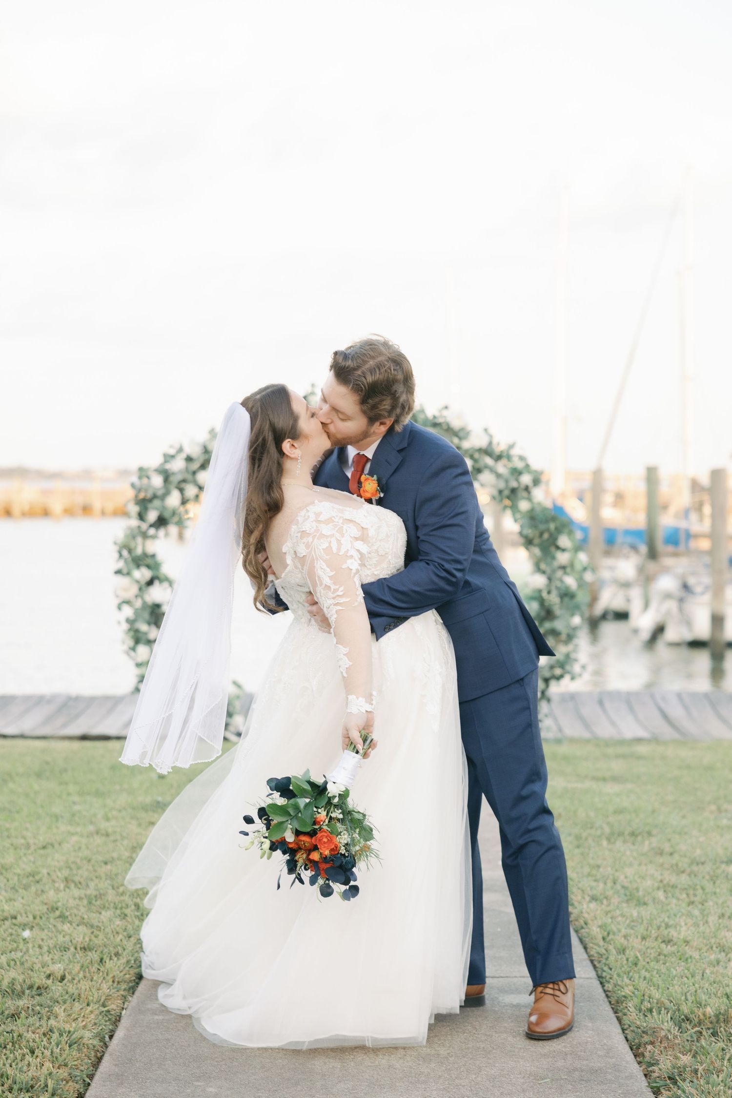 A romantic wedding couple shares intimate moments in a garden setting with flowing white dress and navy suit.