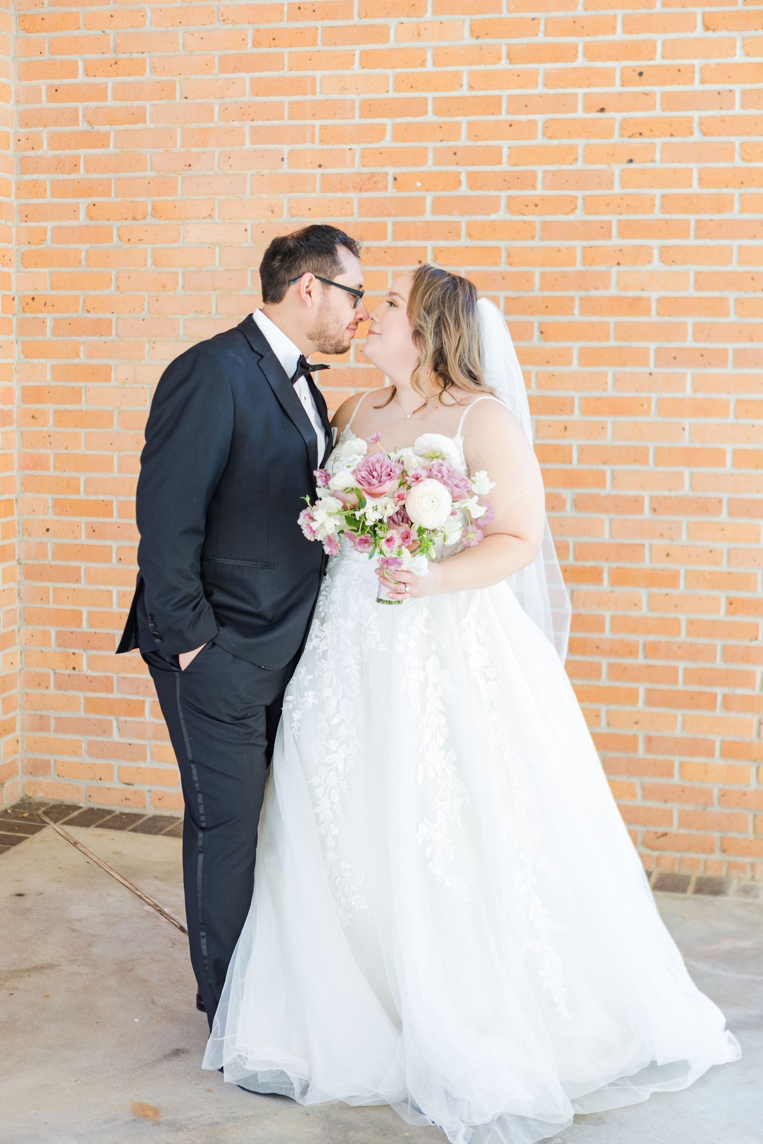 Romantic wedding portraits against orange brick wall with bride in full ballgown.