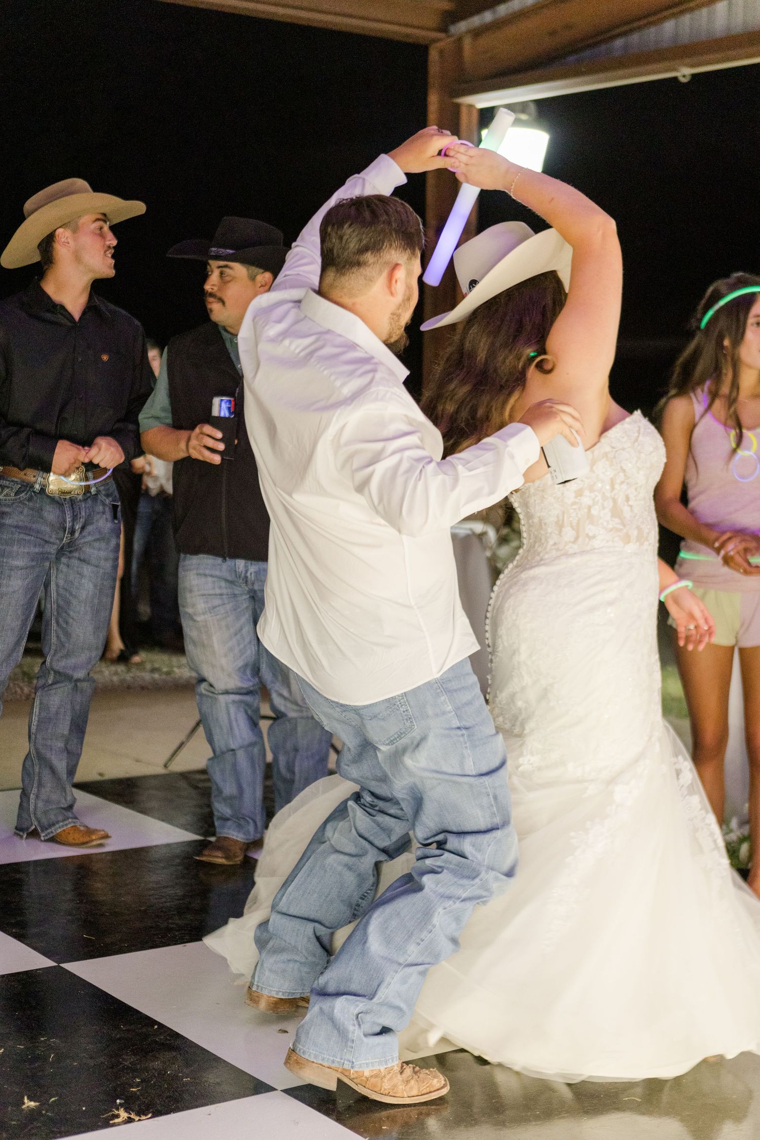 Dancers perform energetic moves on a dance floor at a country western themed wedding celebration.