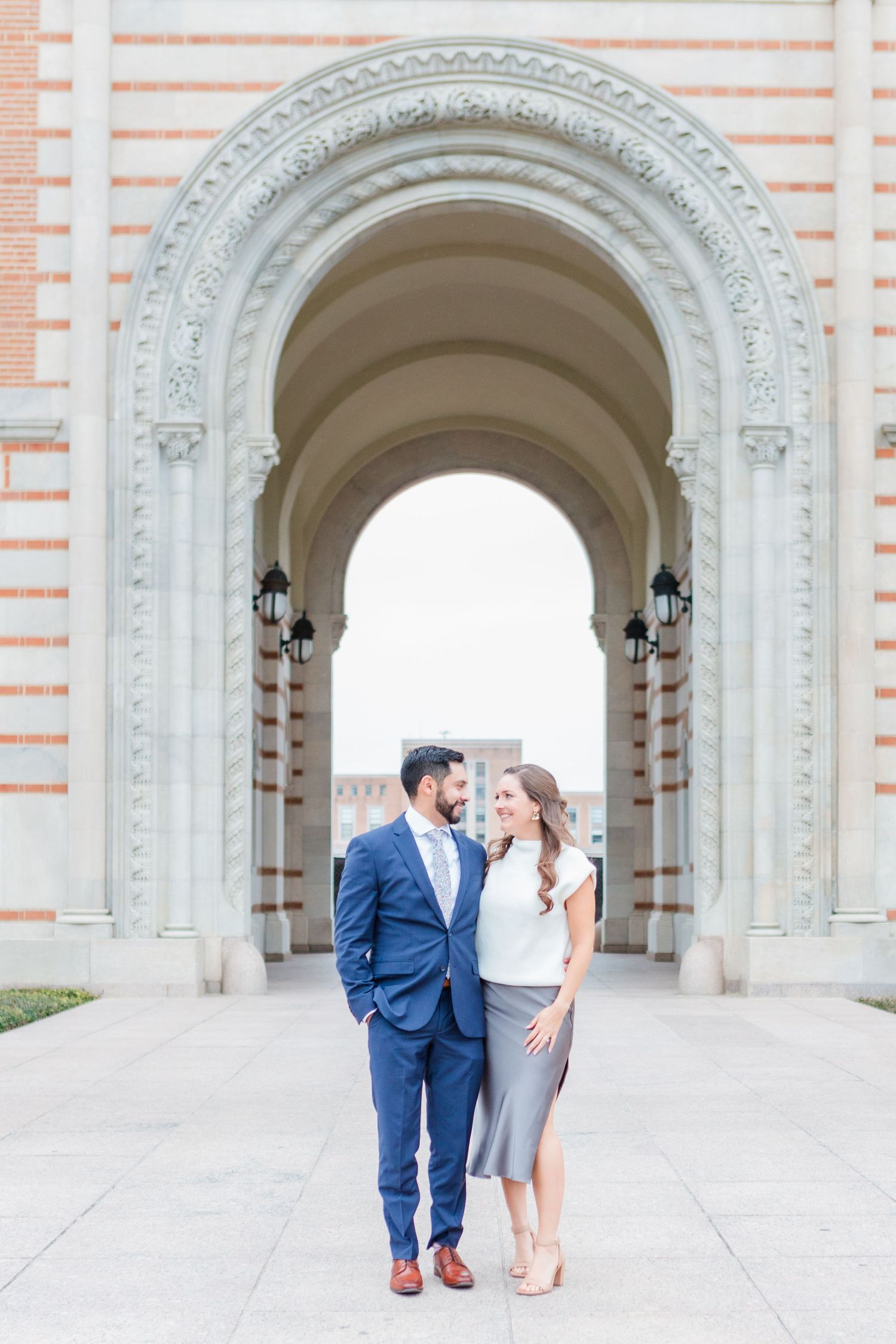 Elegant couple poses under ornate archway of historic building.