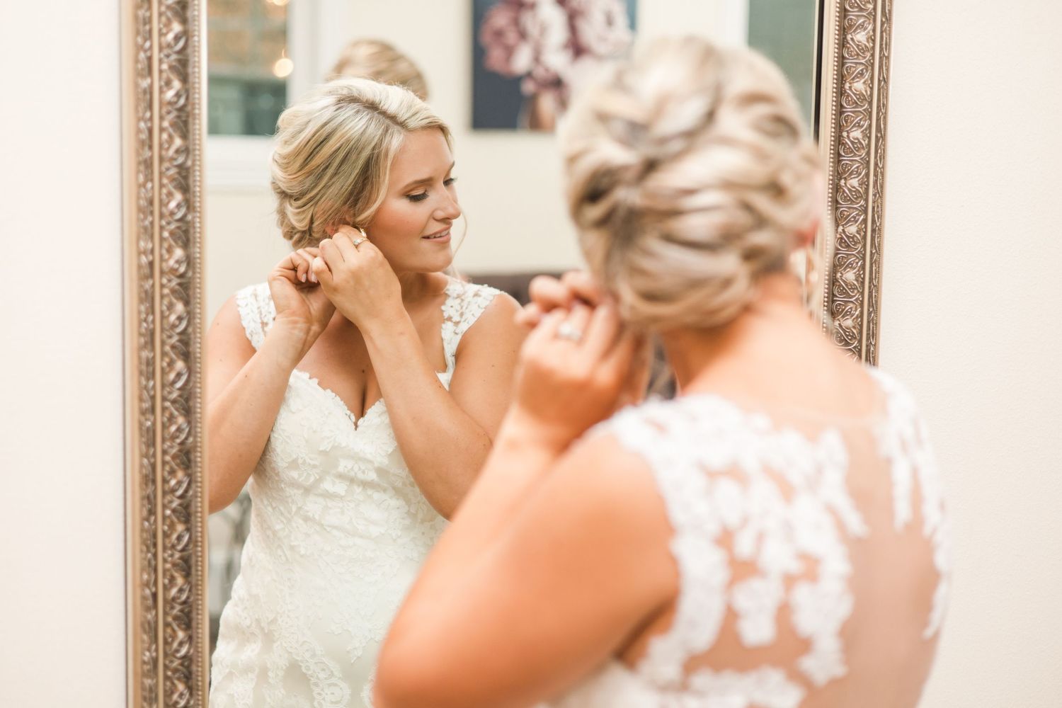 Getting ready scene with elegant wedding dress hanging in ornate mirror reflection.