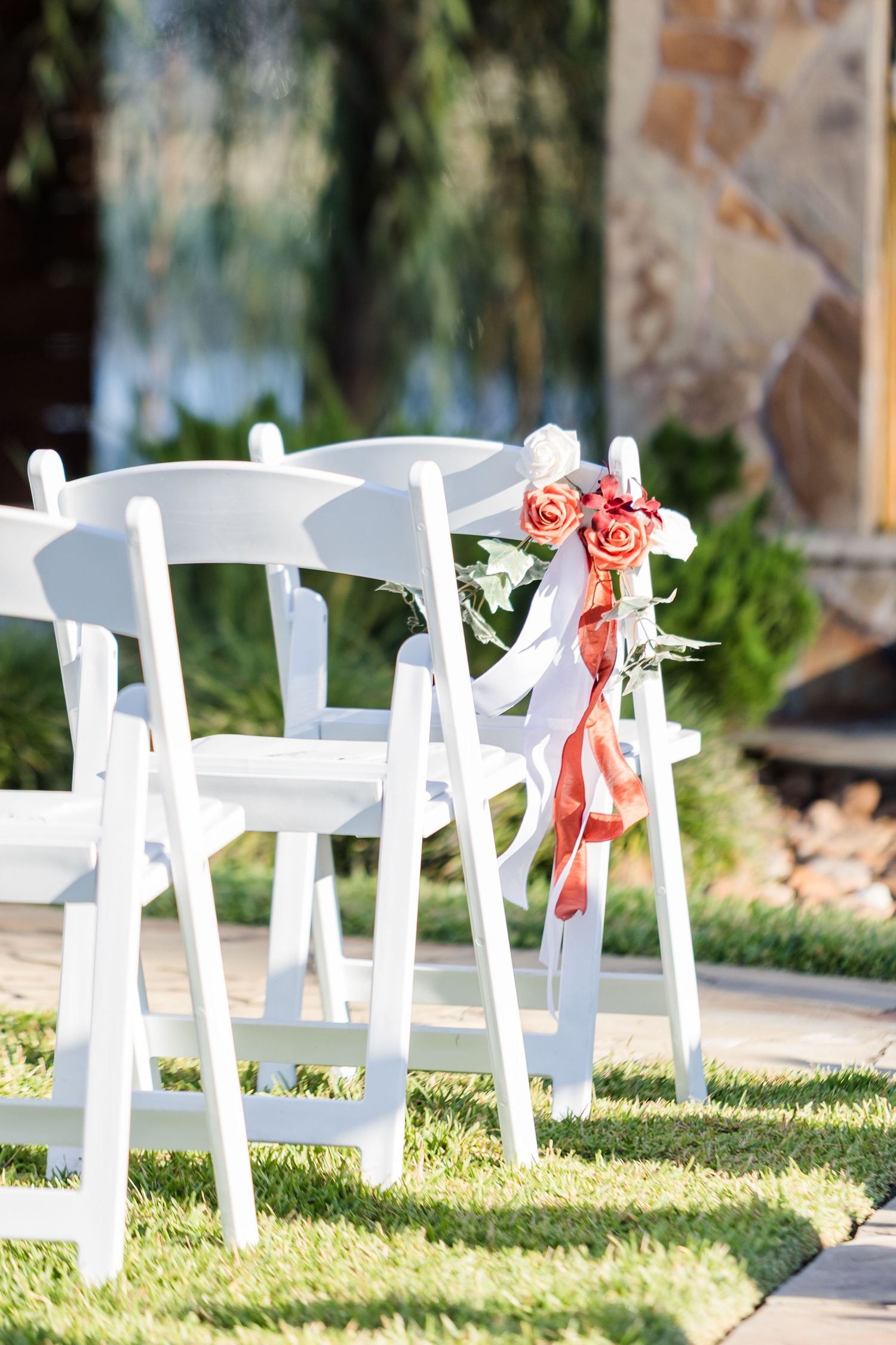 White wooden folding chairs set up on grass for an outdoor wedding ceremony.