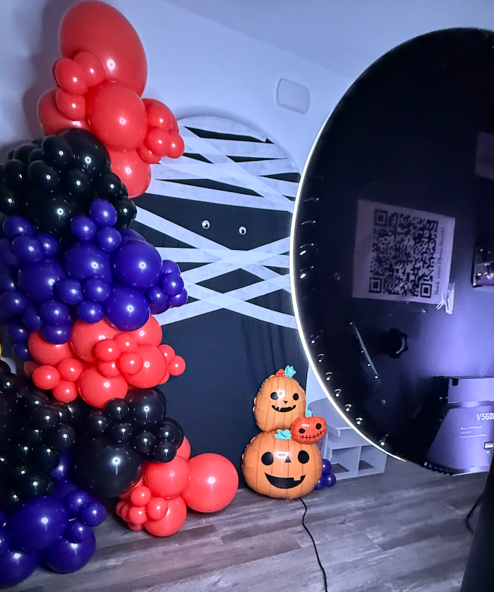 Halloween balloon decorations with orange pumpkins and black and purple balloon arch against a dark wall.