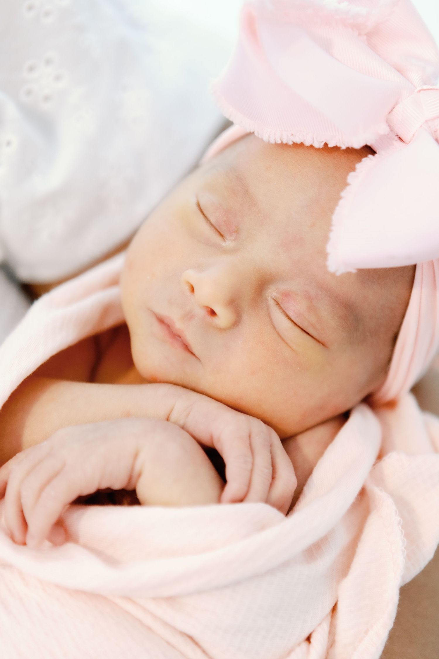 Peaceful sleeping newborn baby wrapped in soft pink blanket with delicate details visible in closeup.