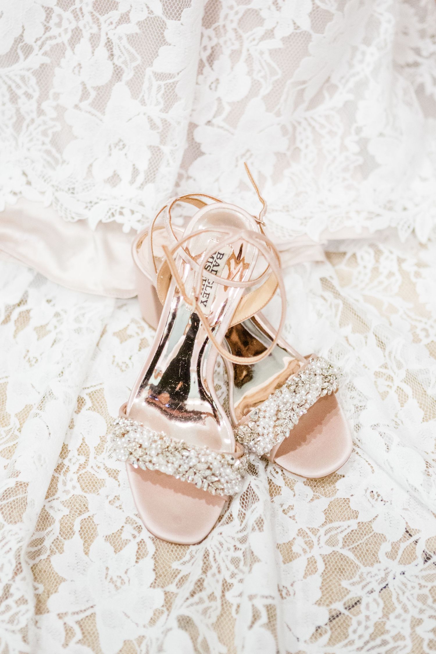 Sparkly blush pink bridal heels displayed on delicate white lace fabric.