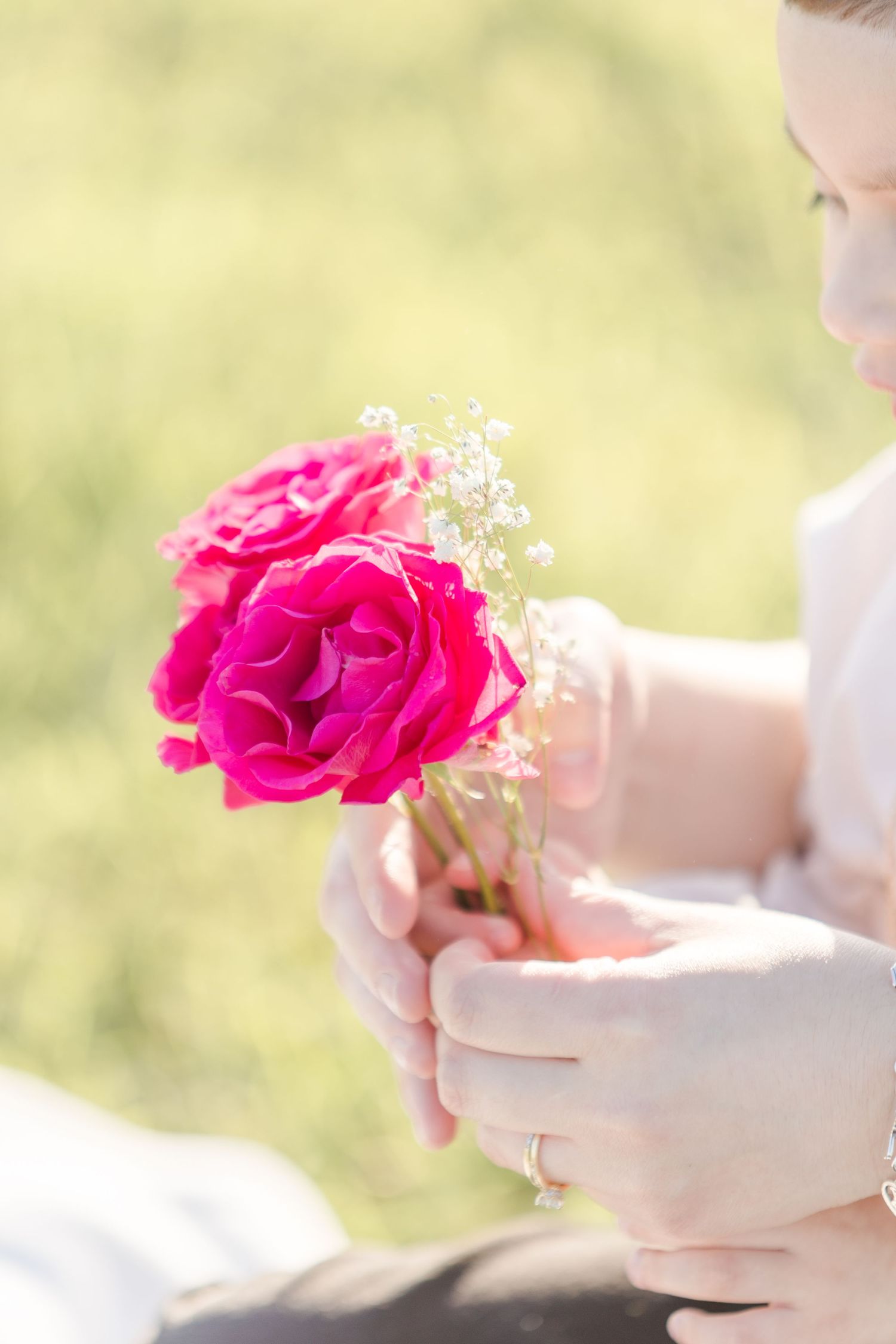 Hands holding bright pink roses against soft blurred background.