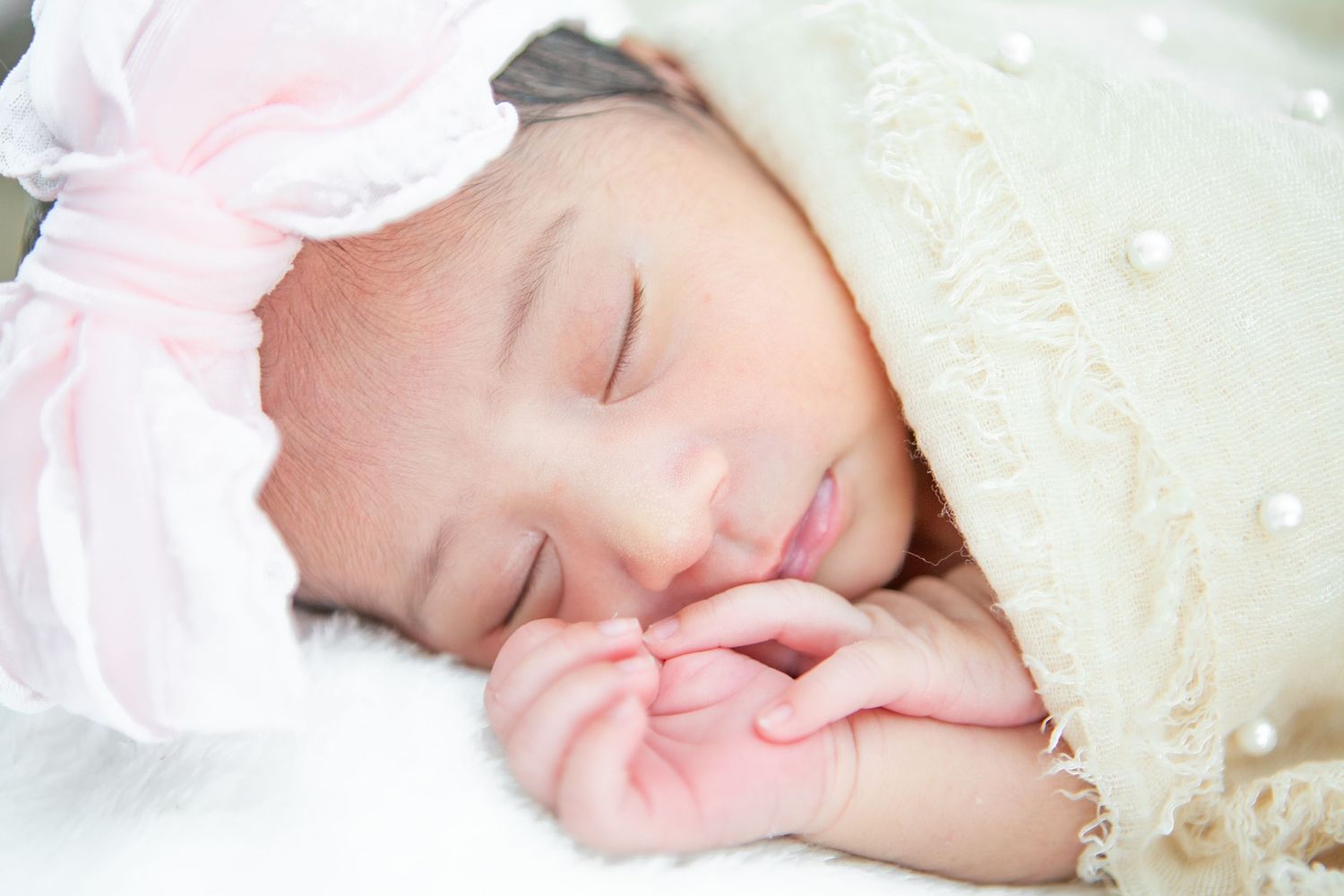 Sleeping infant wrapped in delicate lace fabric against light background.