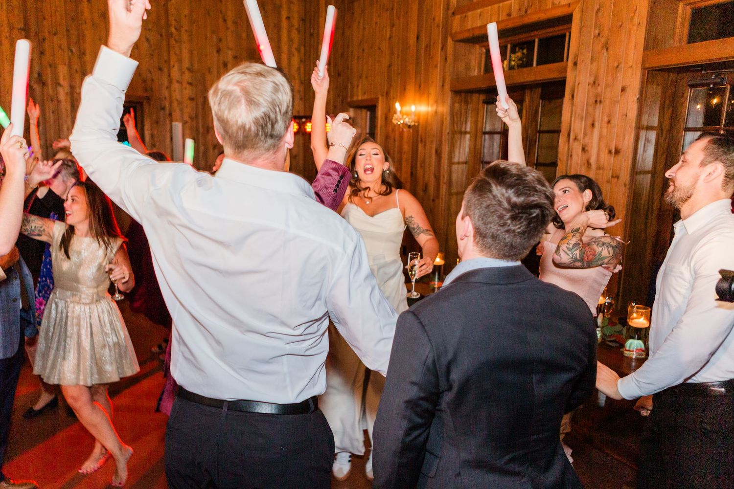 Wedding guests raise their hands in celebration on a crowded dance floor.