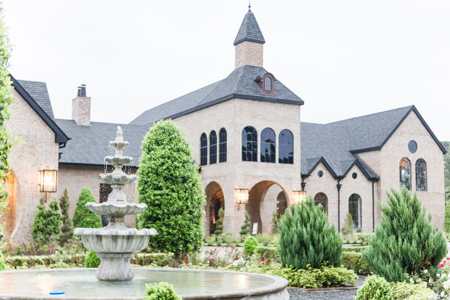 Elegant stone church building with arched windows and decorative fountain in manicured gardens.