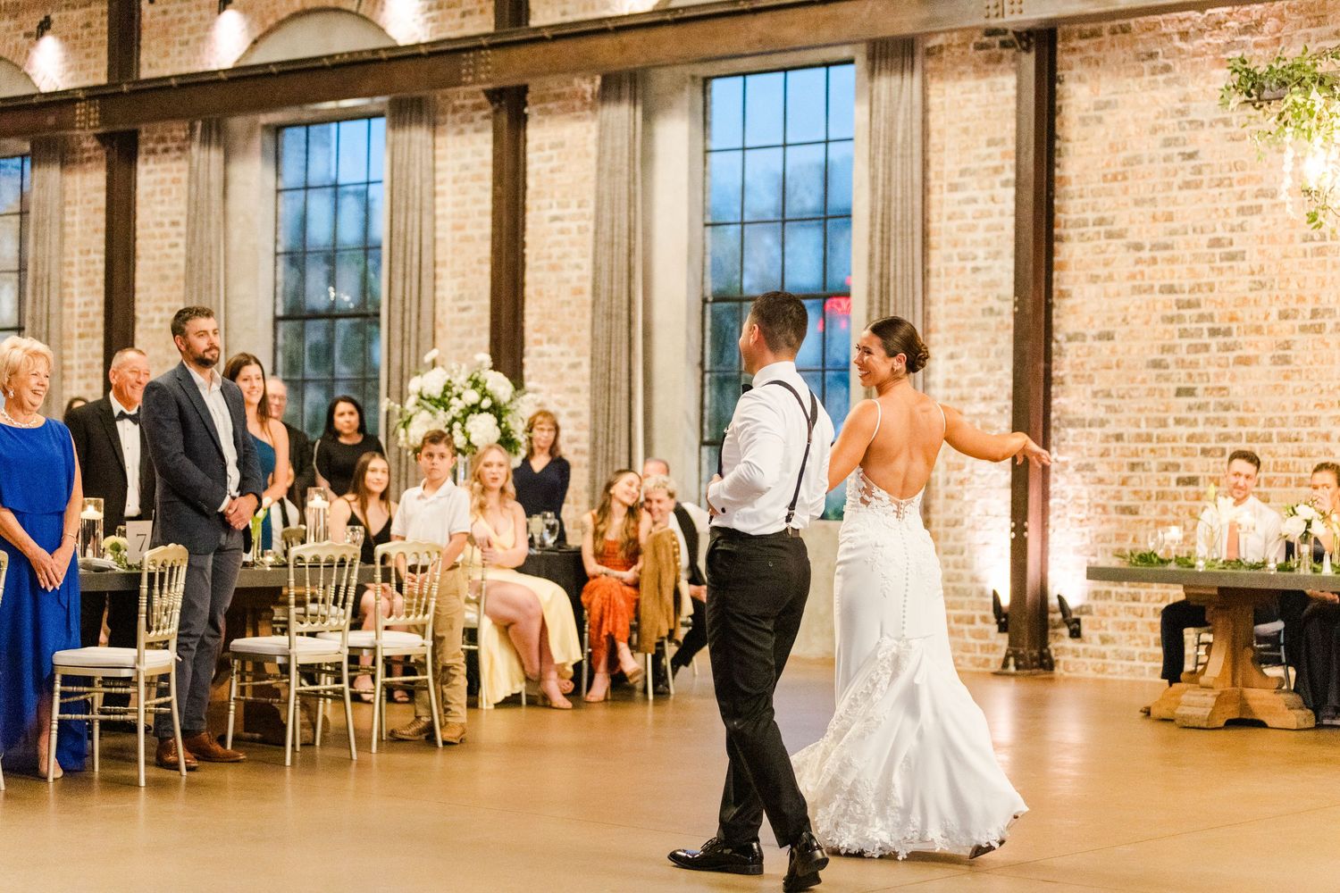 Couples dancing during a wedding reception in a converted industrial space with tall windows.