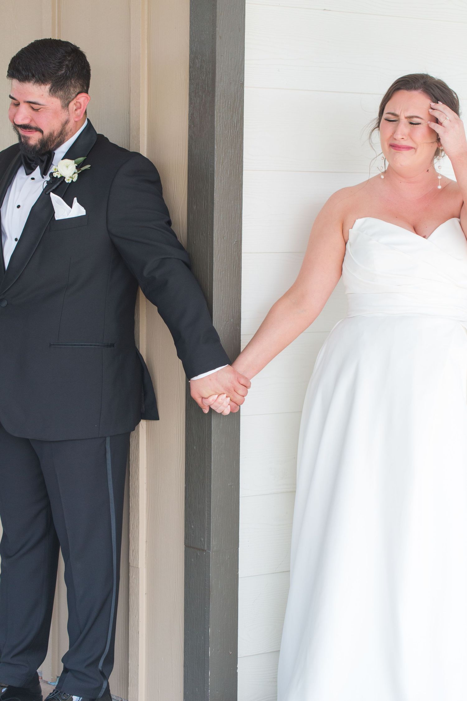 Wedding couple shares a playful moment while standing against a white pillar.